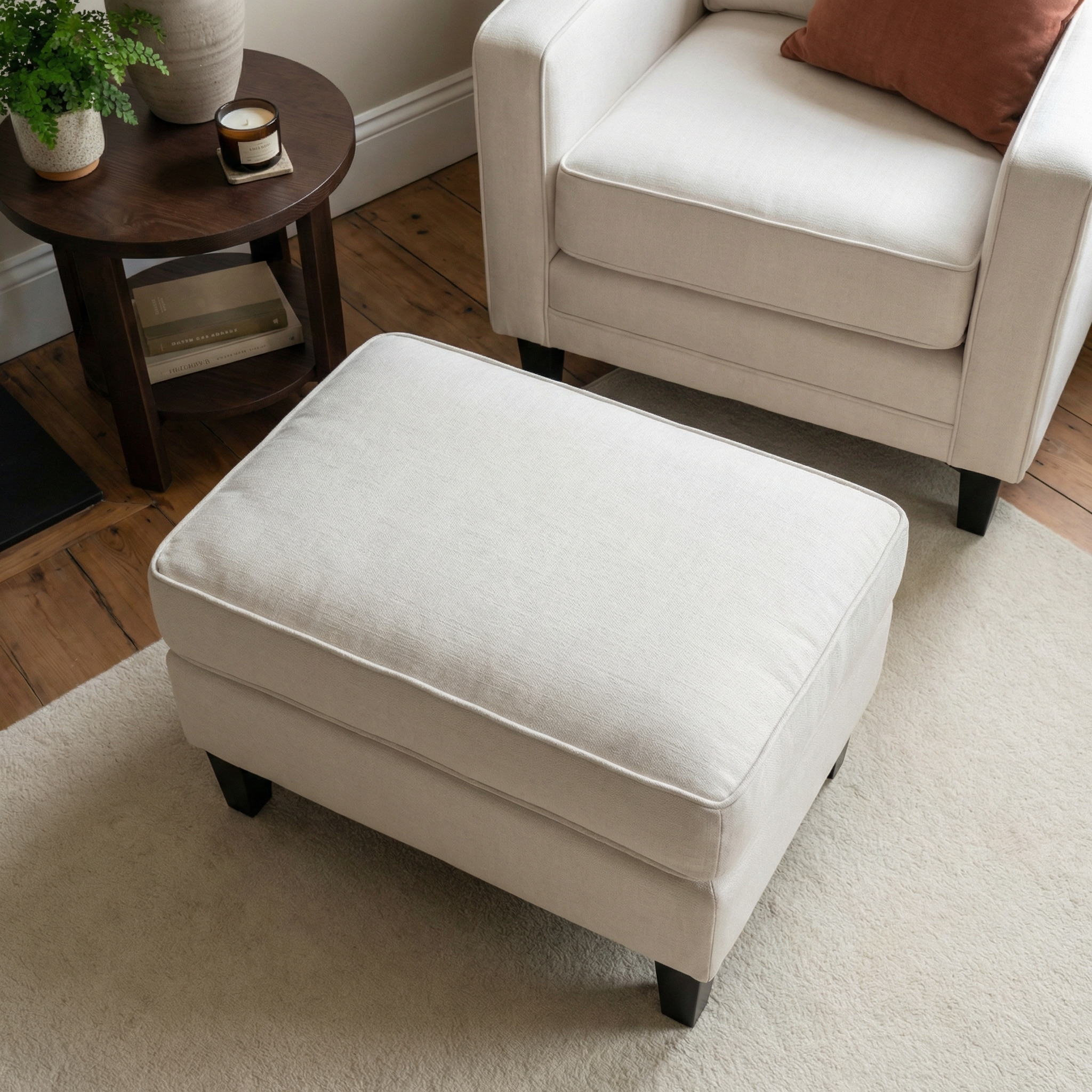 Wiltshire Footstool in Ivory on a beige rug, placed beside a matching armchair and a small round side table with decorative accents.