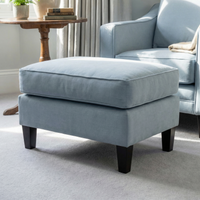 The Wiltshire Footstool in Sky Blue with dark wooden legs sits in a living room near a matching armchair and side table.