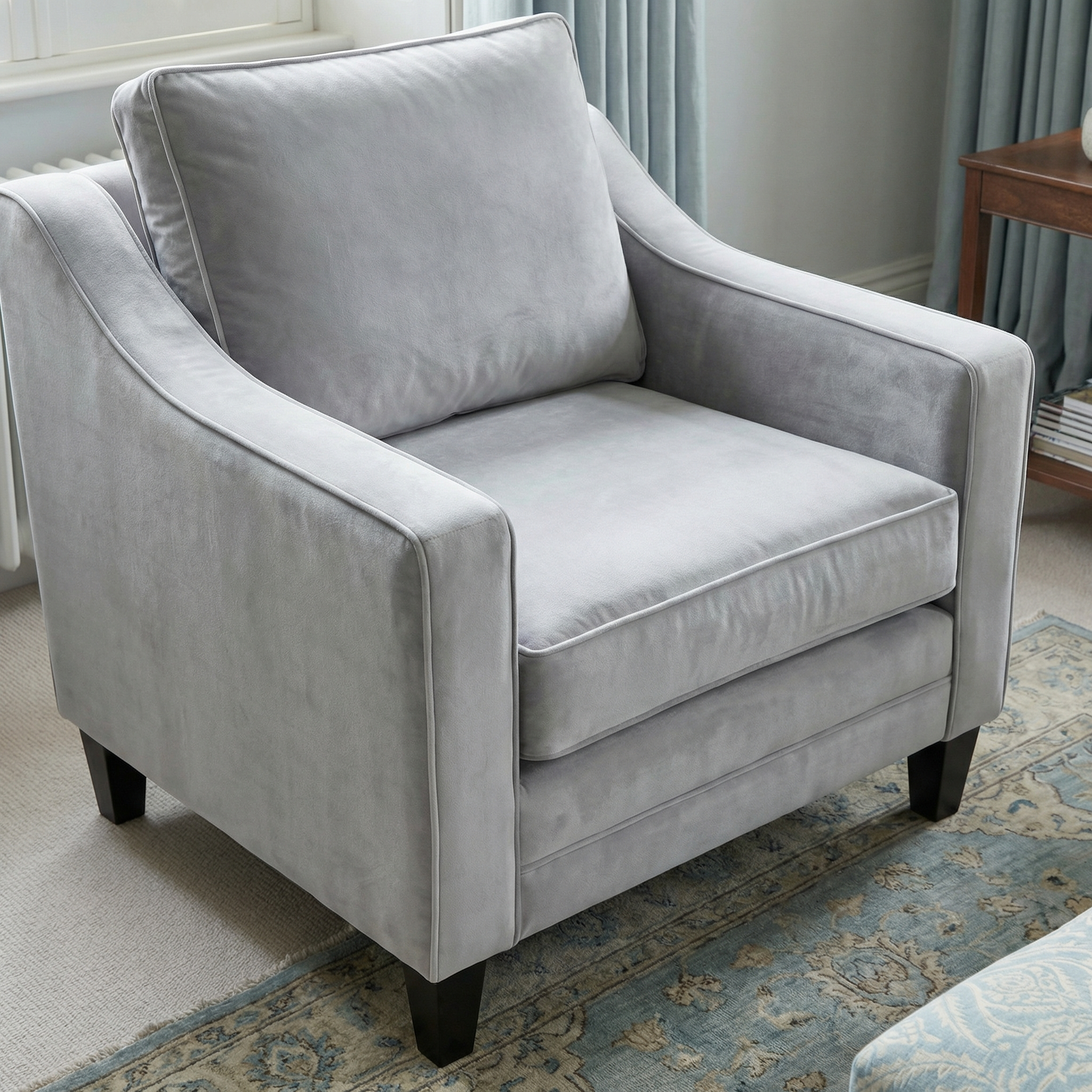 The Wiltshire Velvet Armchair in Feather Grey features light gray upholstery and dark wooden legs, adding elegance to any bright living room.
