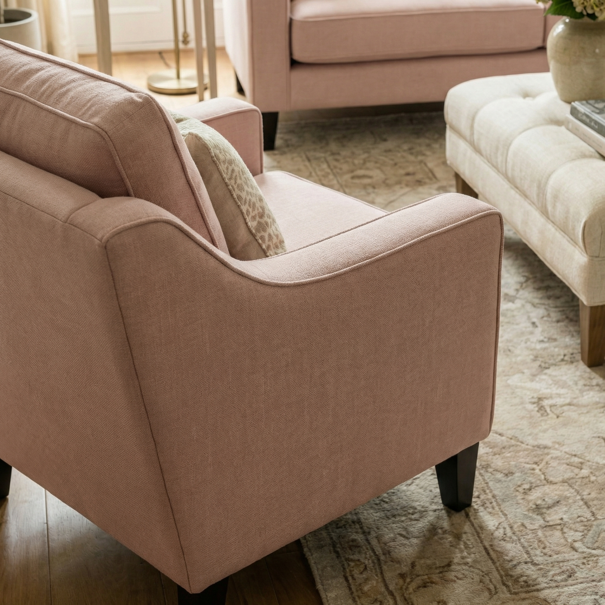 The Wiltshire Armchair in Dusky Pink sits beside a beige ottoman in a cozy, sunlit living room.