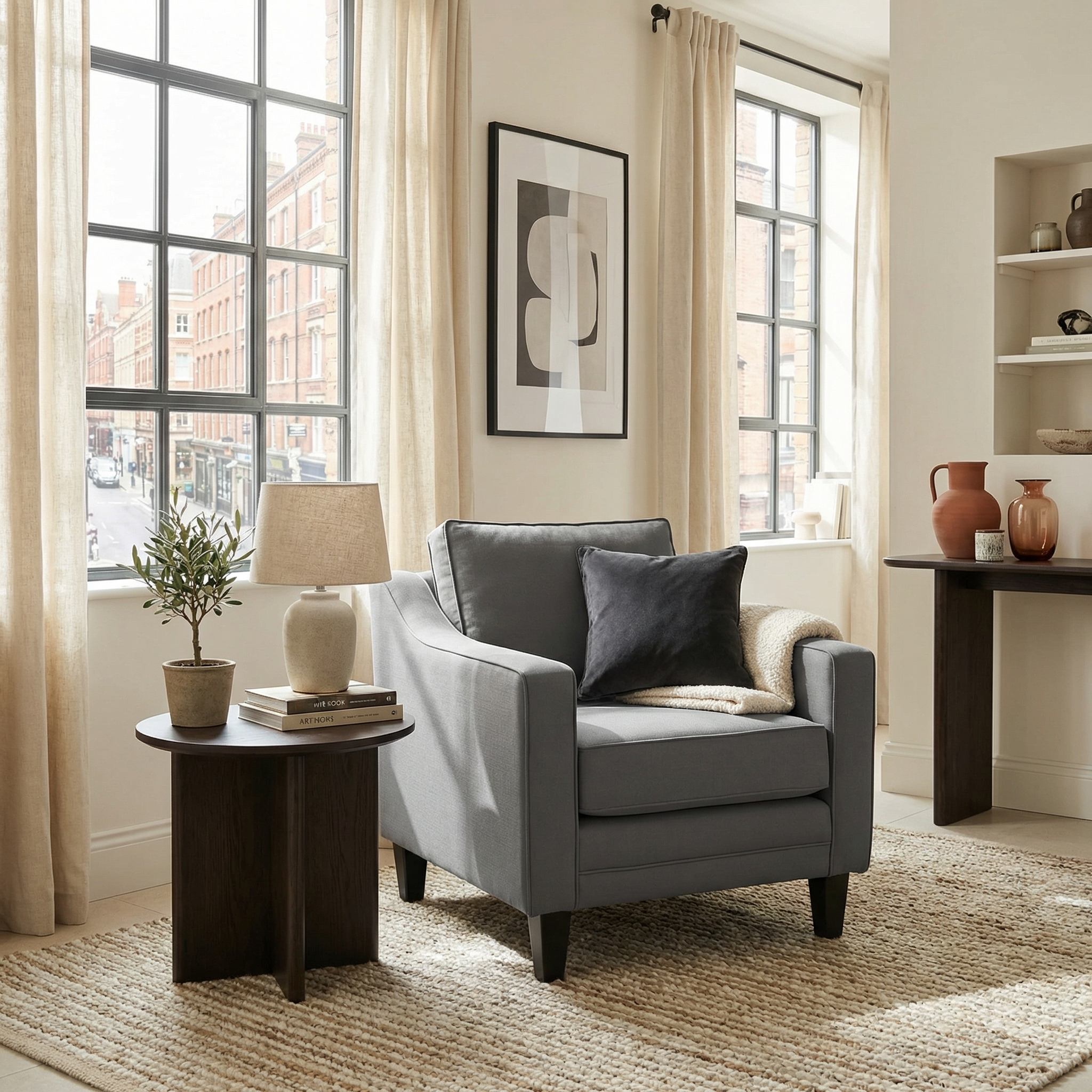 A cozy, modern living room featuring the Wiltshire Armchair in Smoke Grey, paired with a sleek side table, lamp, and large sunny windows.