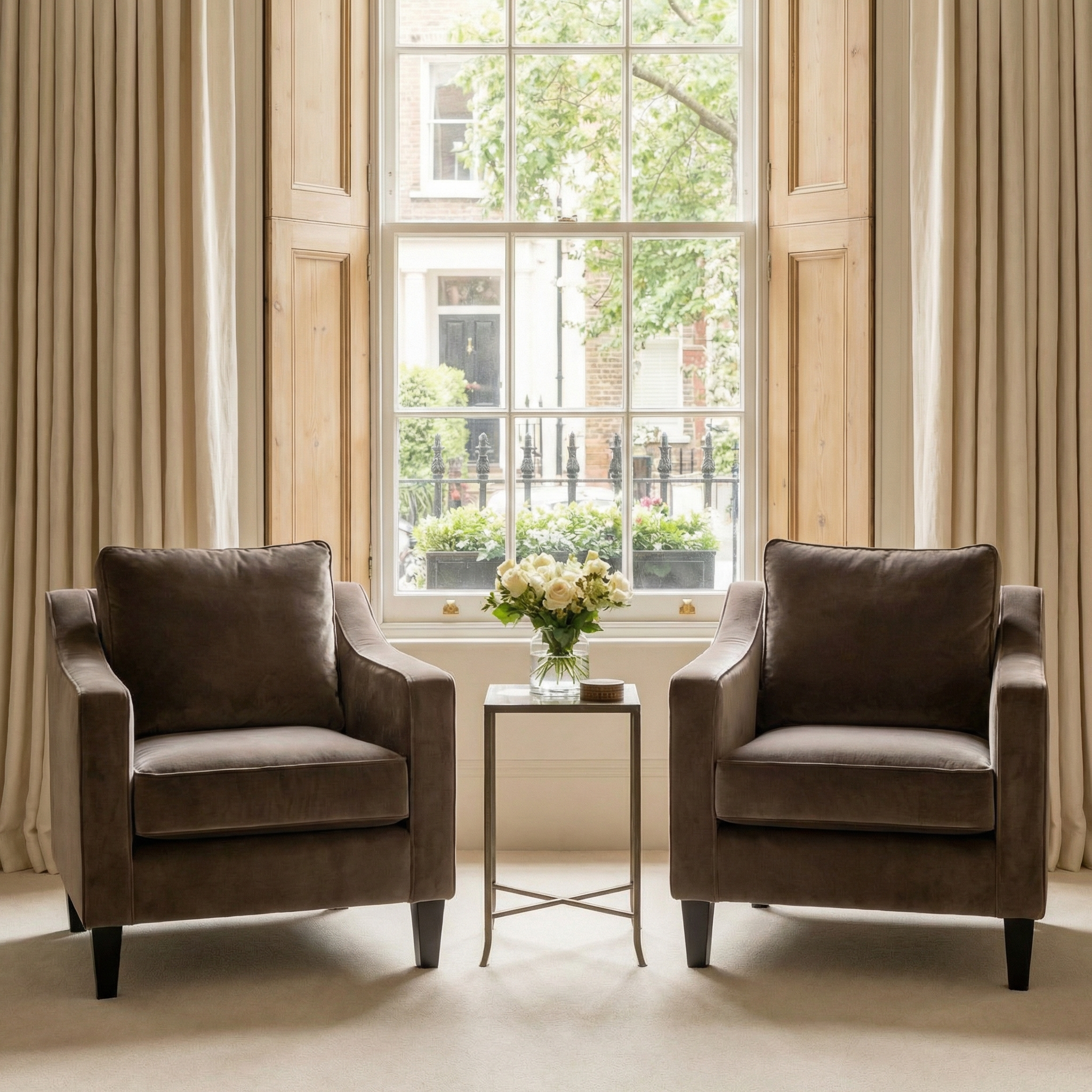 Two Wiltshire Velvet Armchairs in Mink with a small table and flower vase between them, placed in front of a large bright window.