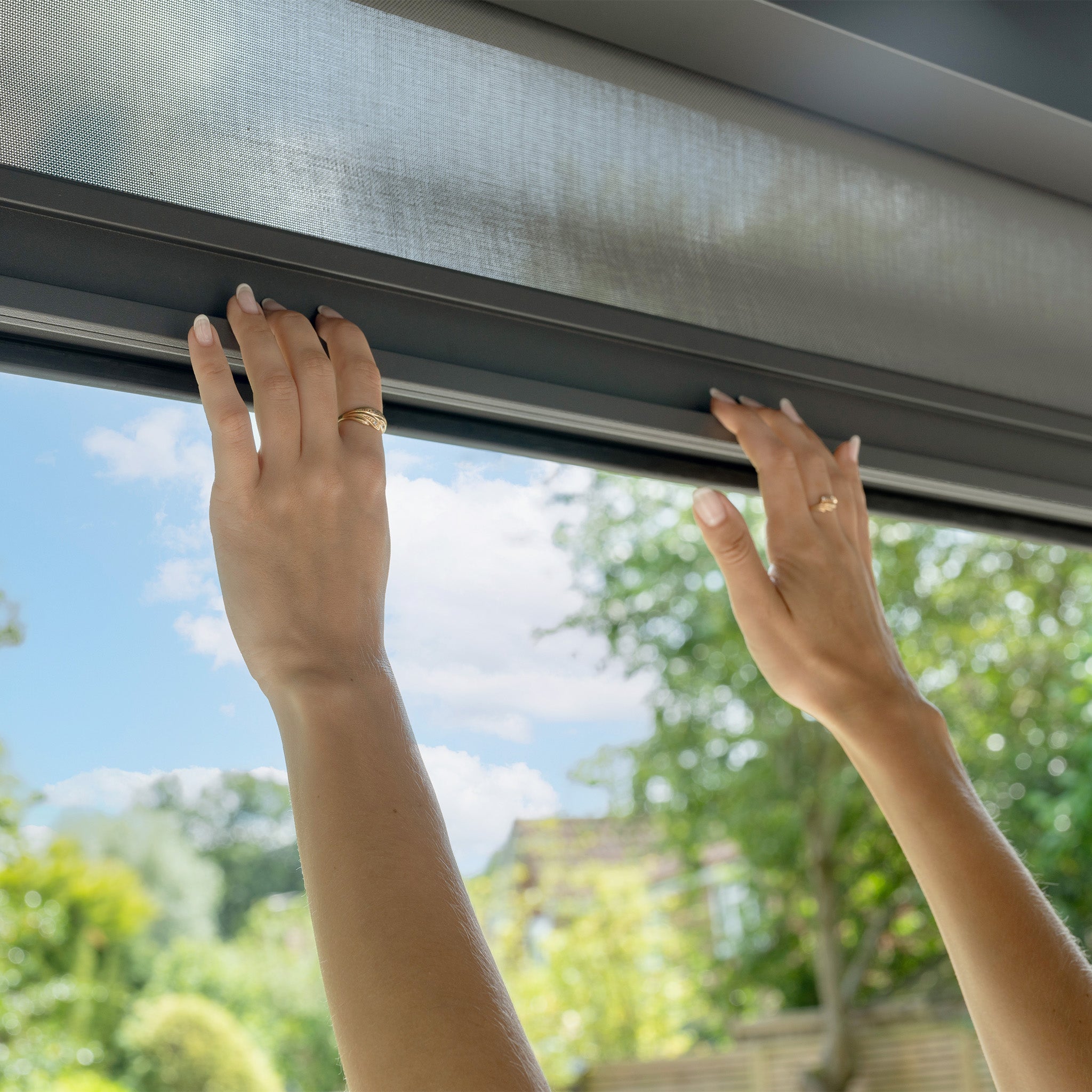 Hands adjusting a window blind with a garden view echo the sleek, modern ambience of the PergoSTET Plus 3m x 4m Rectangular Pergola, featuring adjustable louvres, wood effect finish, LED lighting, and 3 drop sides.