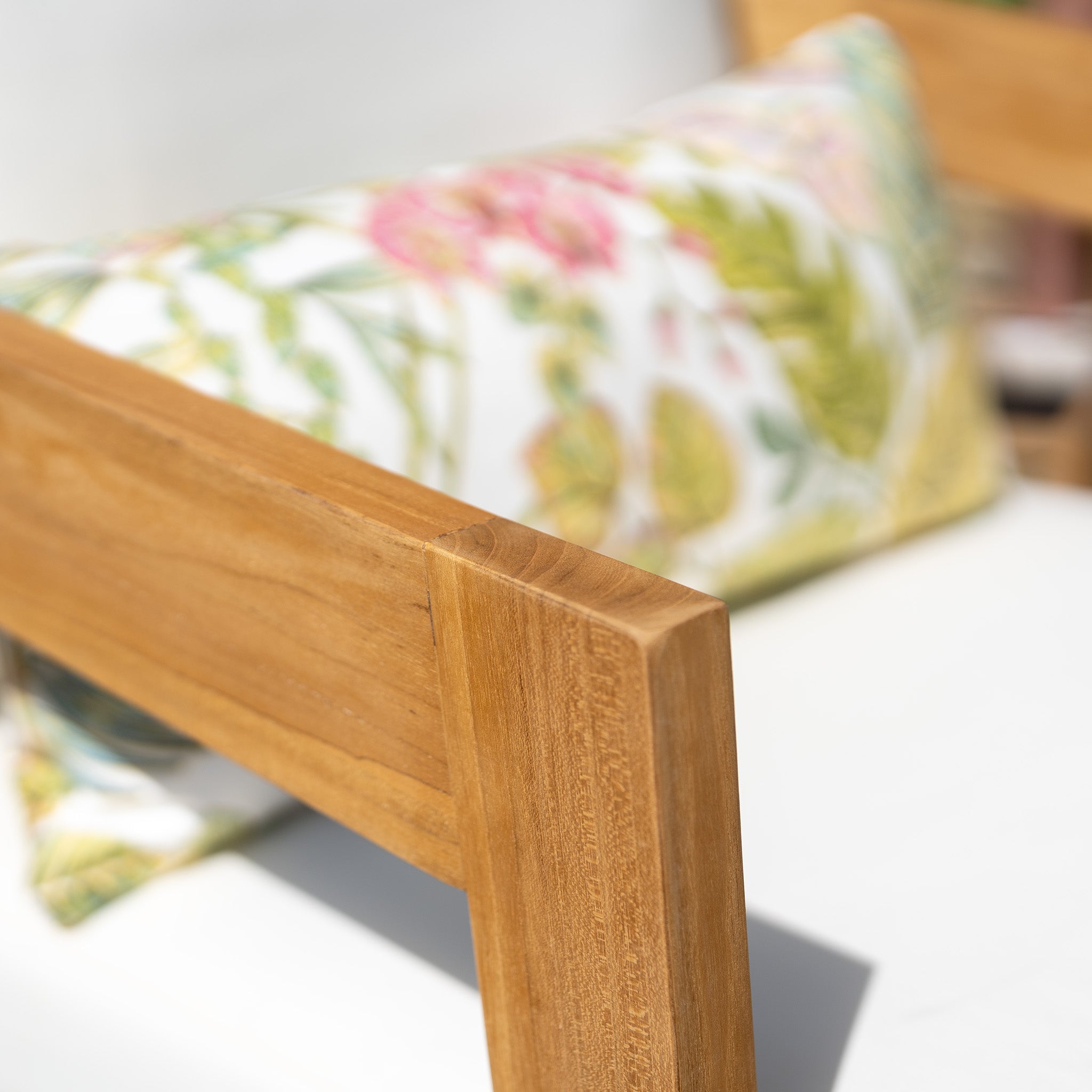 Close-up of a Yosemite 2 Seat Sofa Set In Glacier, showcasing its finely crafted premium teak wood construction and adorned with a vibrant floral cushion made from water-resistant polyester fabric, set against a light-colored backdrop.