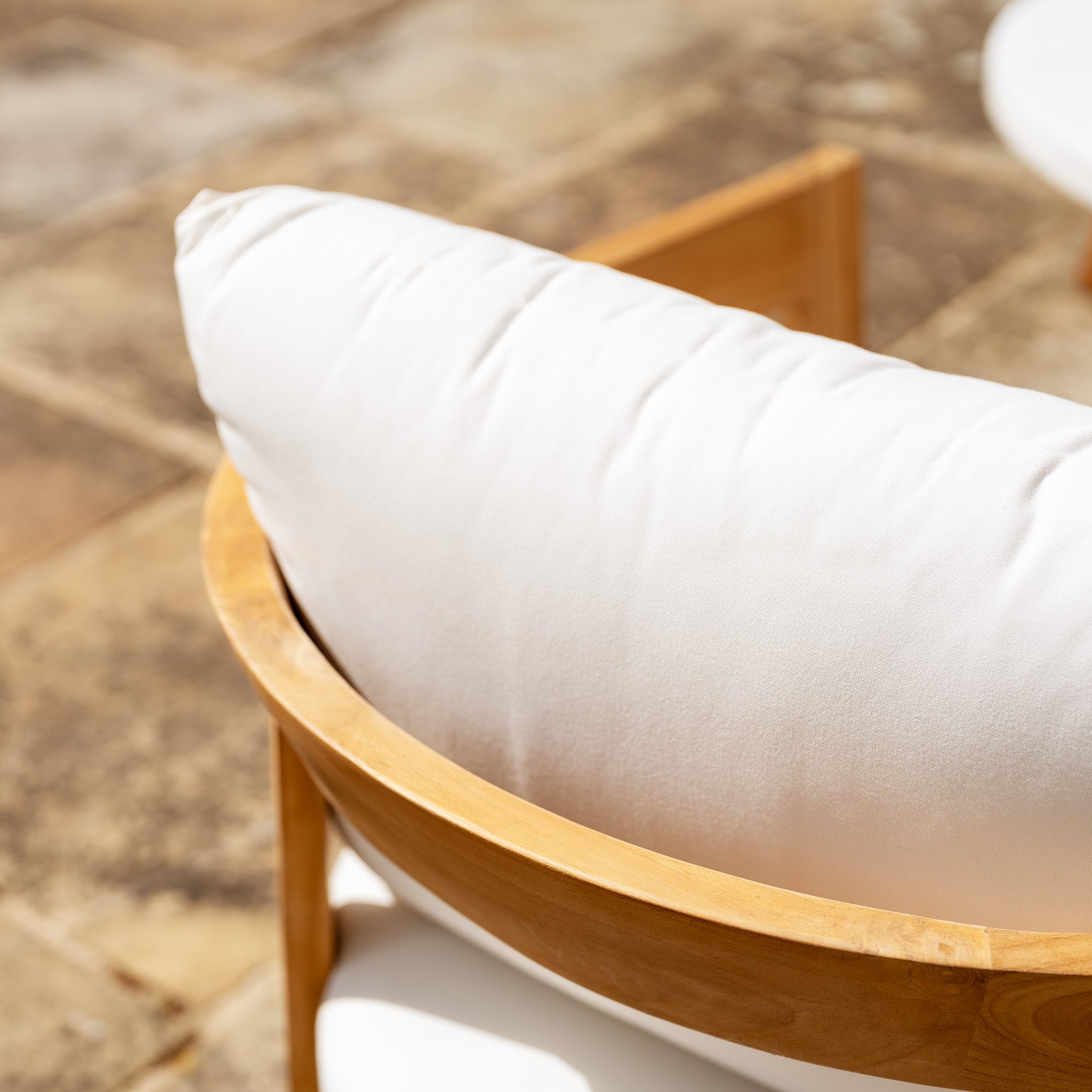 Close-up of the Yosemite 2 Seat Sofa Set in Glacier from the Yosemite Collection, highlighted by plush white cushions on a stone patio. Crafted from premium teak wood, the sofa set glows in bright sunlight, casting soft shadows.