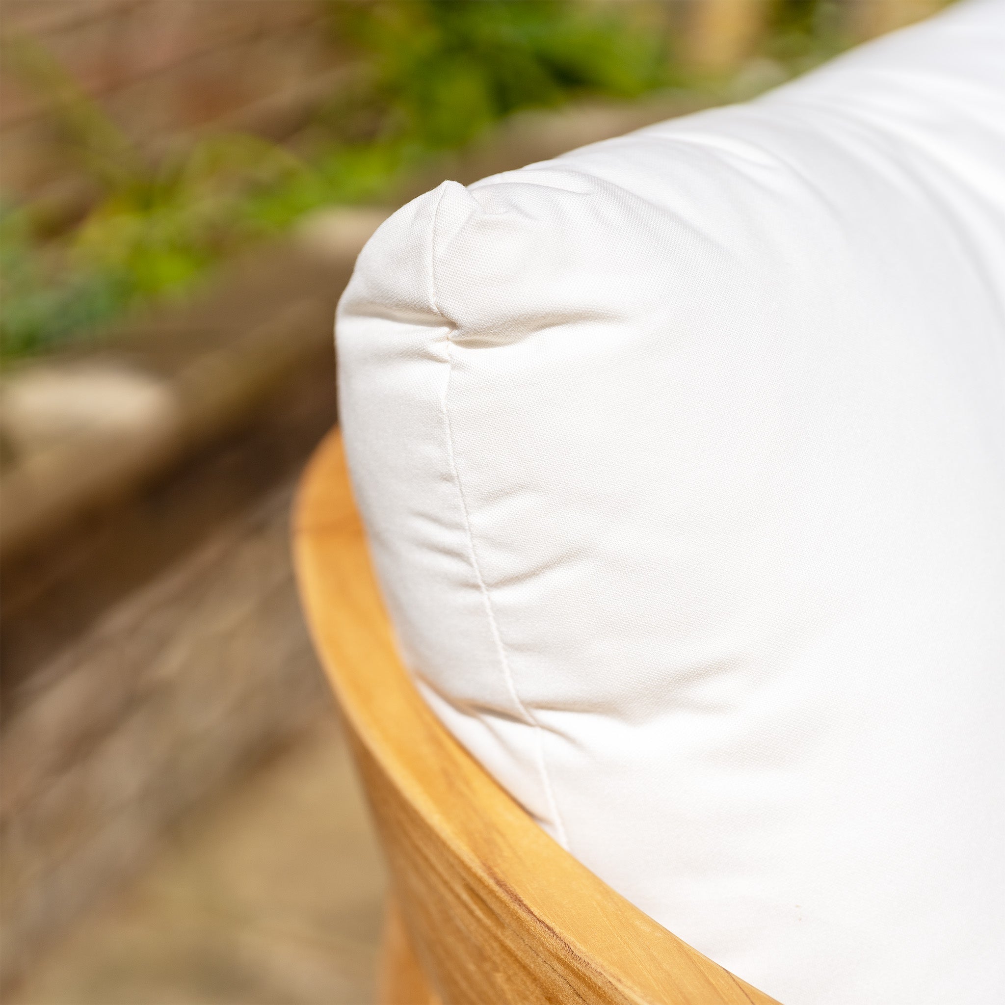 Close-up of a white cushioned pillow on a wooden chair from the Yosemite 3 Seat Sofa Set in Glacier, with a blurred background of a garden area.
