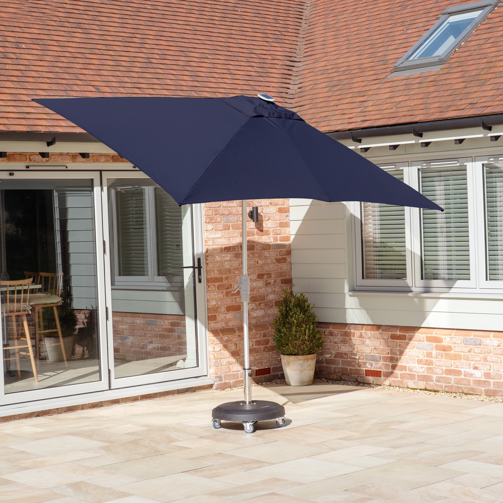 A Zelos 3m x 2m Rectangular Parasol with LED Lighting in Navy stands on a sunny terrace, its pale tiles complementing the modern house.