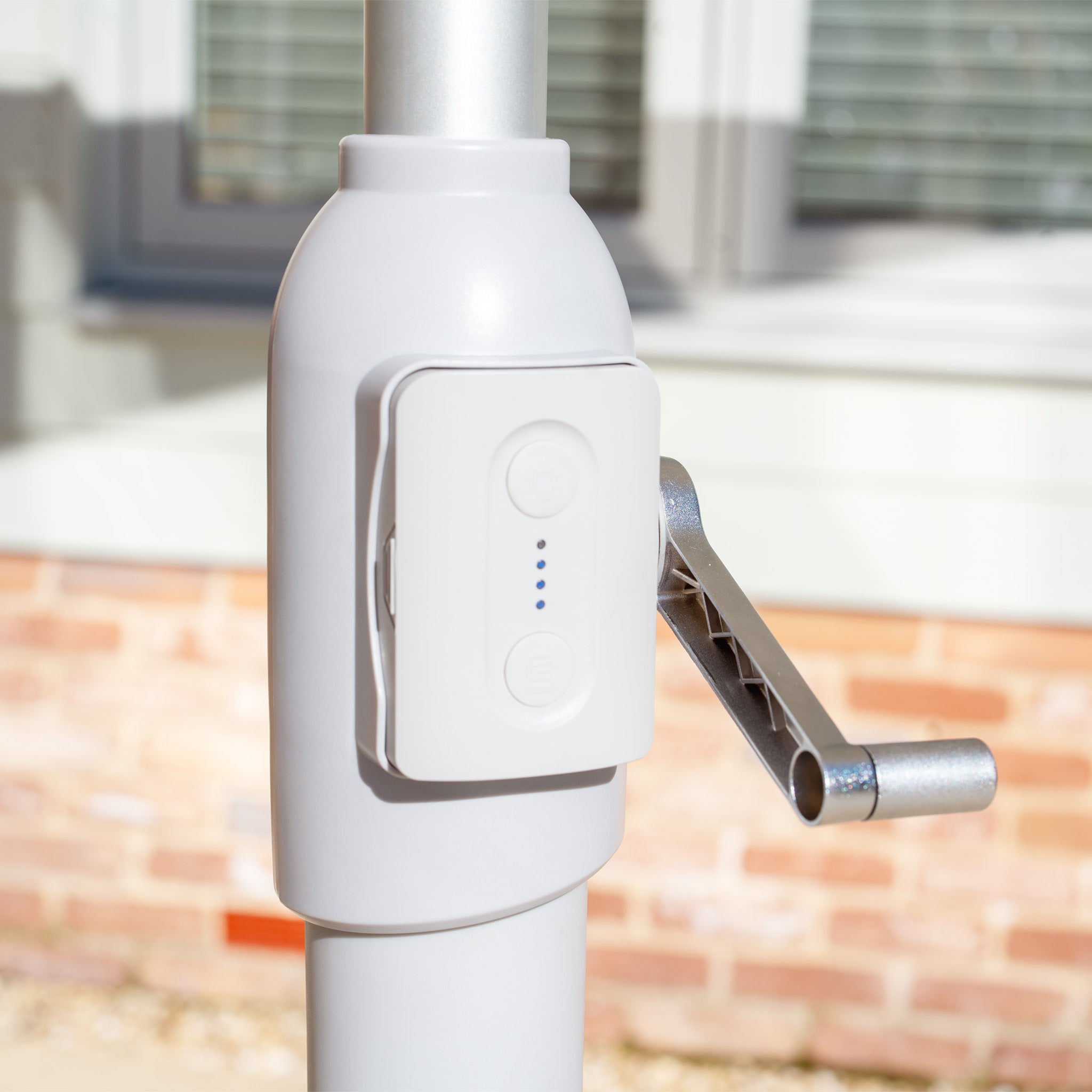 A close-up of a mechanical crank handle on a pole, with the Zelos 2.5M Round Parasol with LED Lighting in Cream providing UV protection in the background, perfect for enhancing outdoor living spaces.