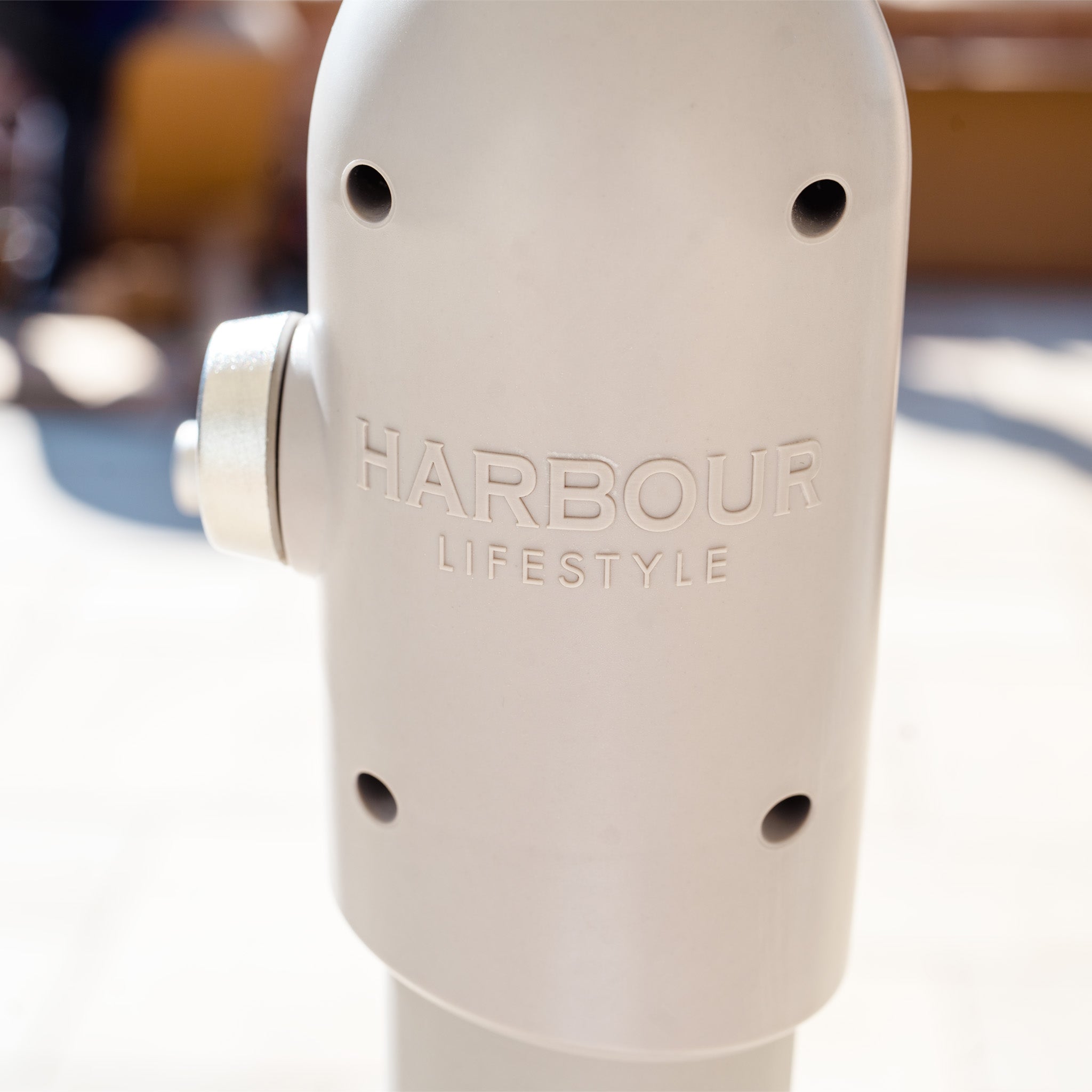 A close-up of a metal object with "Harbour Lifestyle" engraved, casting a sleek reflection beneath the gentle shelter of the Zelos 2.5M Round Parasol with LED Lighting in Green.