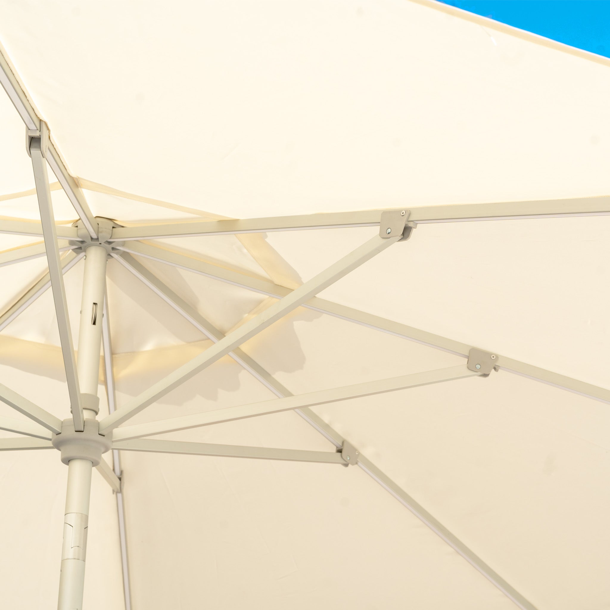 The underside of a cream Zelos 2.5M Round Parasol with UV protection and LED lighting is set against a clear blue sky.