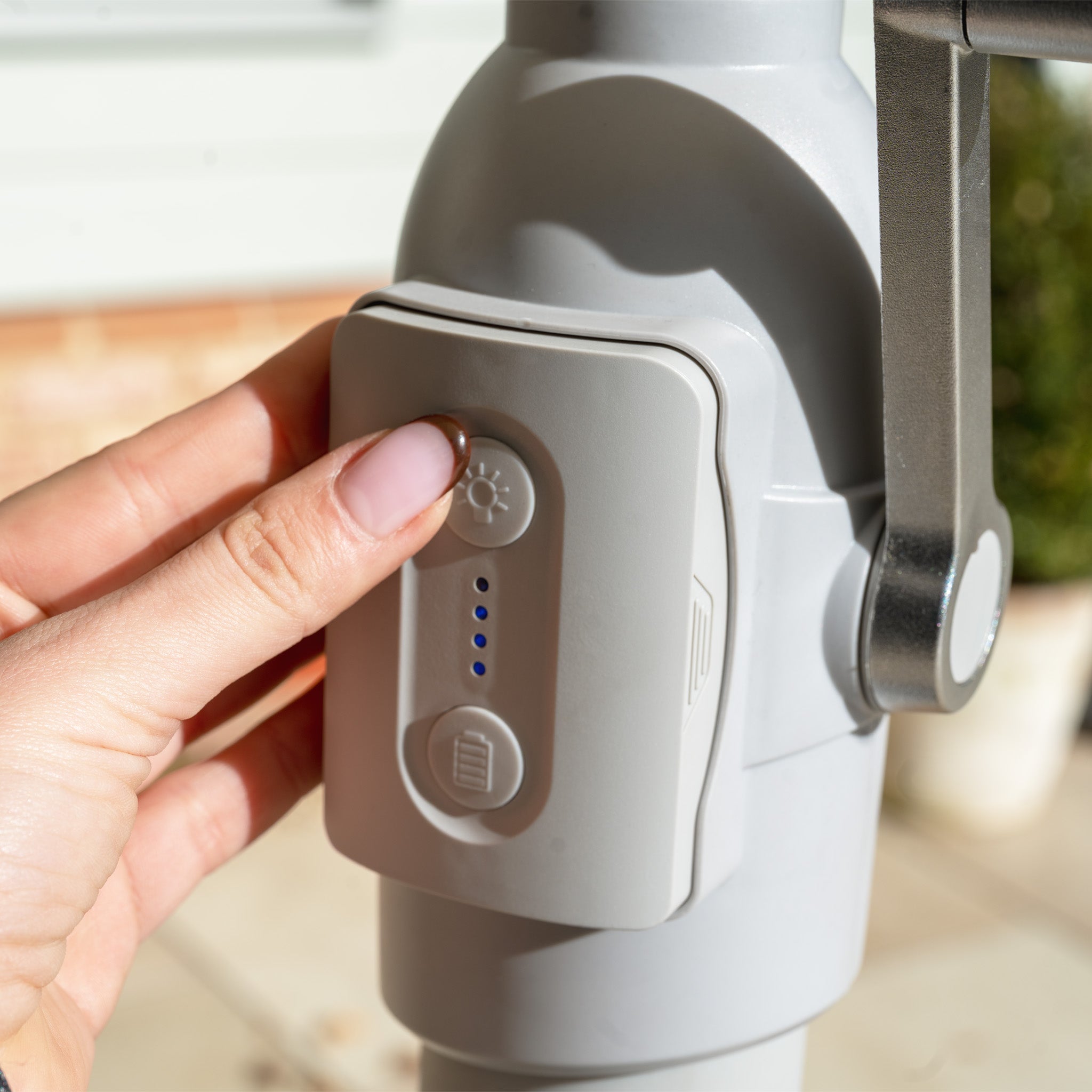 A hand presses a button with light icons on a gray outdoor device, featuring blue LEDs, beneath the Zelos 2.5M Round Parasol with LED Lighting in Navy.