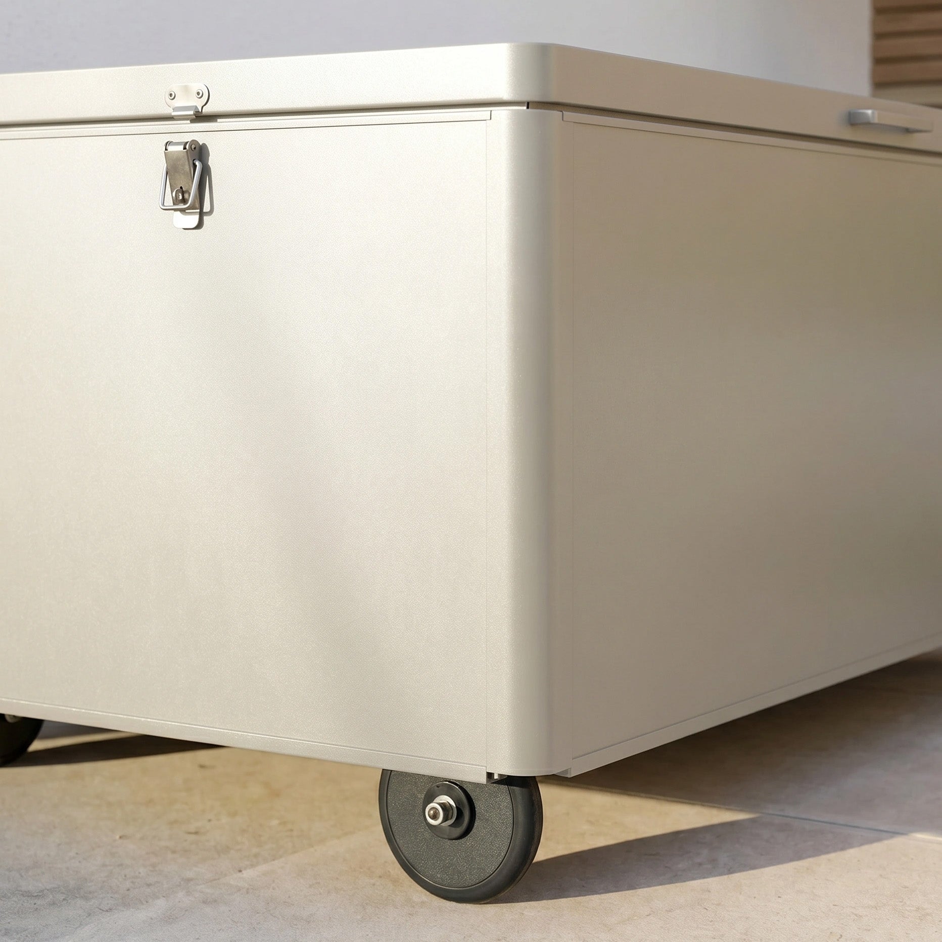 A Large Aluminium Storage Box in Latte with wheels and a latch sits on a light tiled floor—ideal for use as garden storage or as a versatile outdoor storage box.
