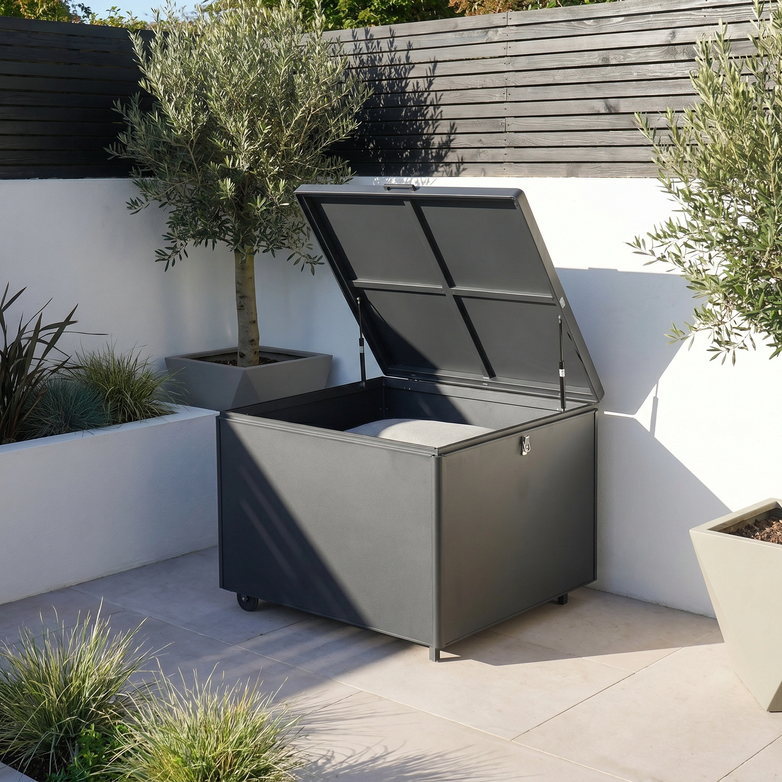 The Small Aluminium Storage Box in Grey, featuring an open lid and wheels, is perfect for waterproof garden storage on patios, complementing olive trees and white walls.