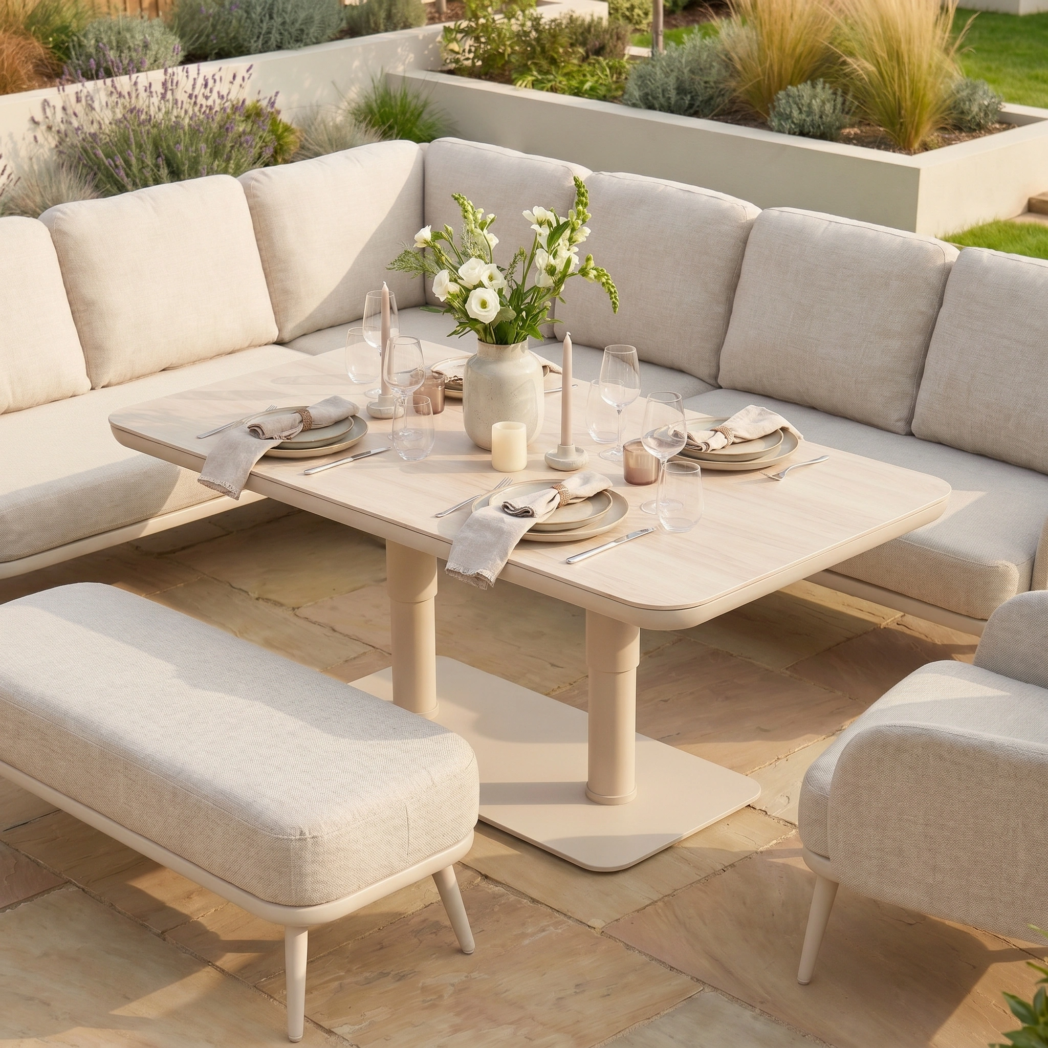 The Alva Corner Dining Set with Rising Table and Armchair in Fawn, set for four with plates, glasses, and a floral centerpiece—stylish garden furniture for elegant outdoor dining.