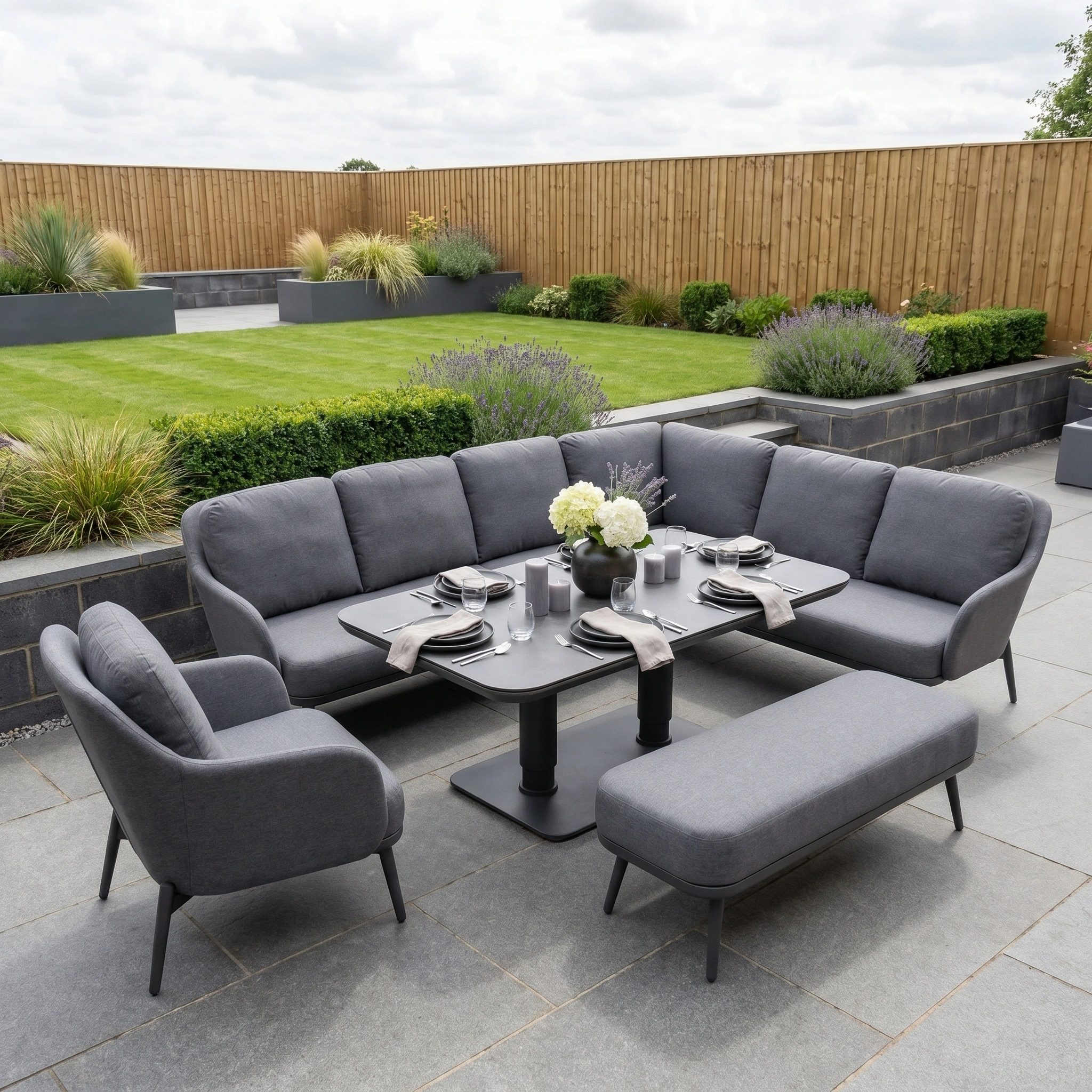 The Alva Corner Dining Set with Rising Table and Armchair in Grey is ideal for relaxing in your landscaped garden with grass and wooden fencing.