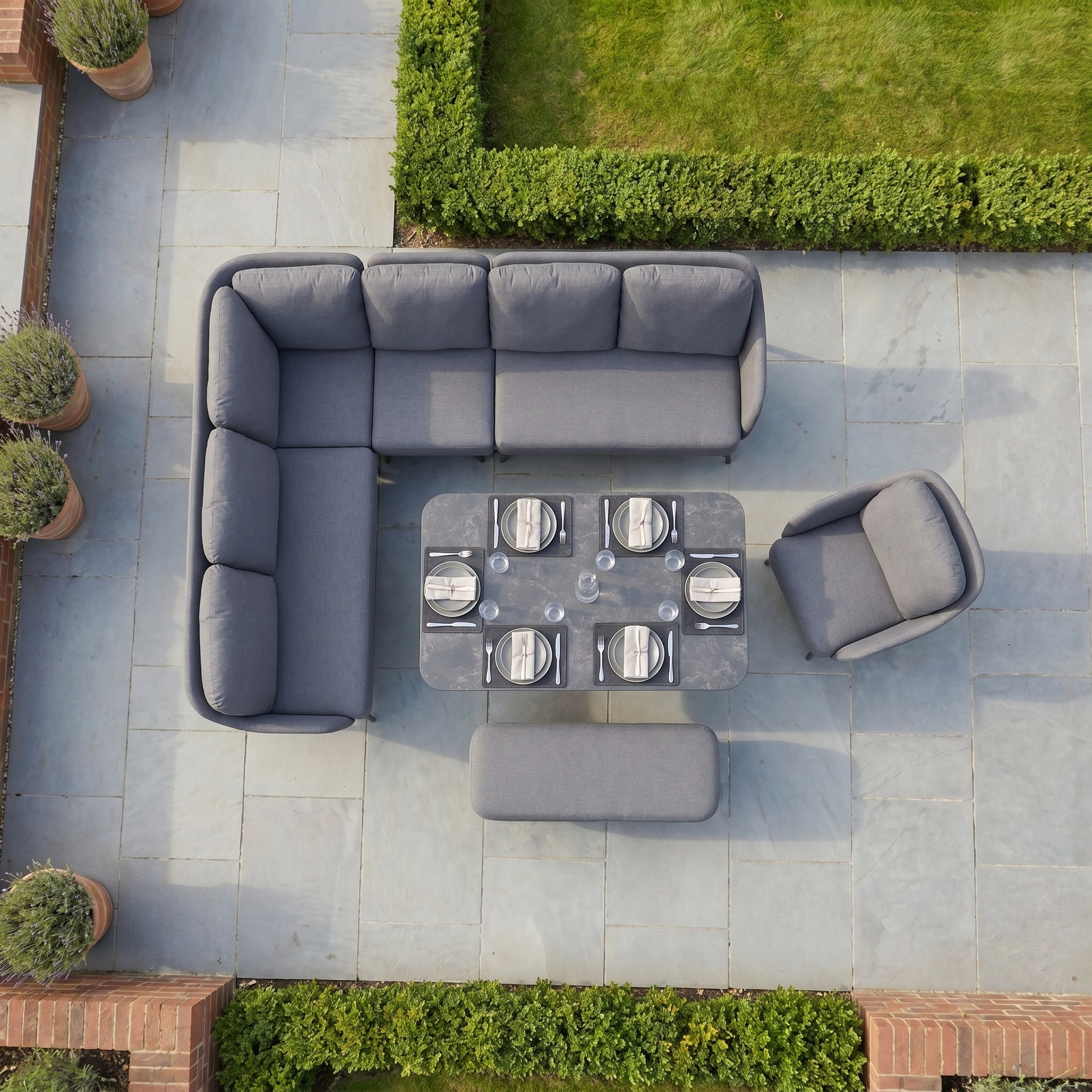 Aerial view of the Alva Corner Dining Set with Rising Table and Armchair in Grey, featuring plates, surrounded by garden hedges.