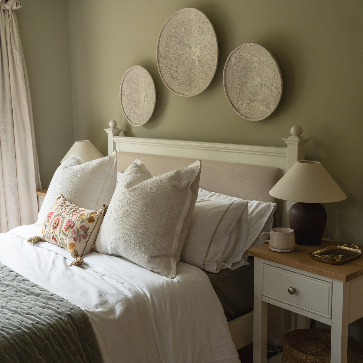 Cozy bedroom featuring the Amberley 5ft Kingsize Bed Frame in Warm White with white bedding, two side tables, lamps, and three round wall decorations above the upholstered headboard.