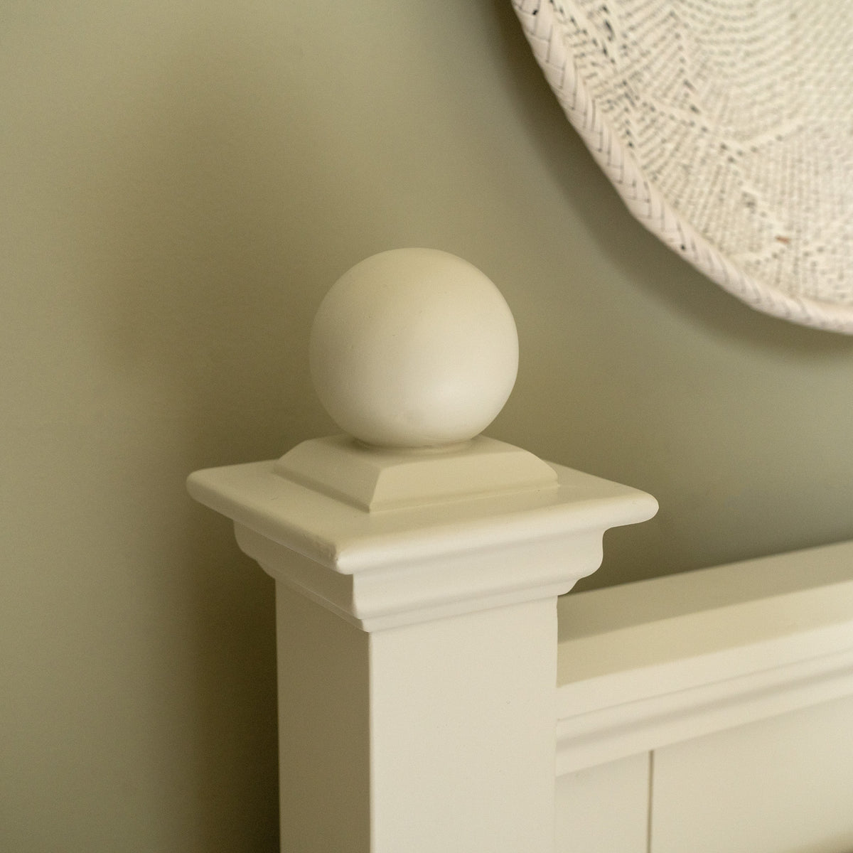 Amberley 5ft Kingsize Bed Frame in Warm White features a white bedpost with a decorative round finial, shown in front of a beige wall and woven wall art—a stylish wooden bed that complements any upholstered headboard or kingsize bedroom décor.