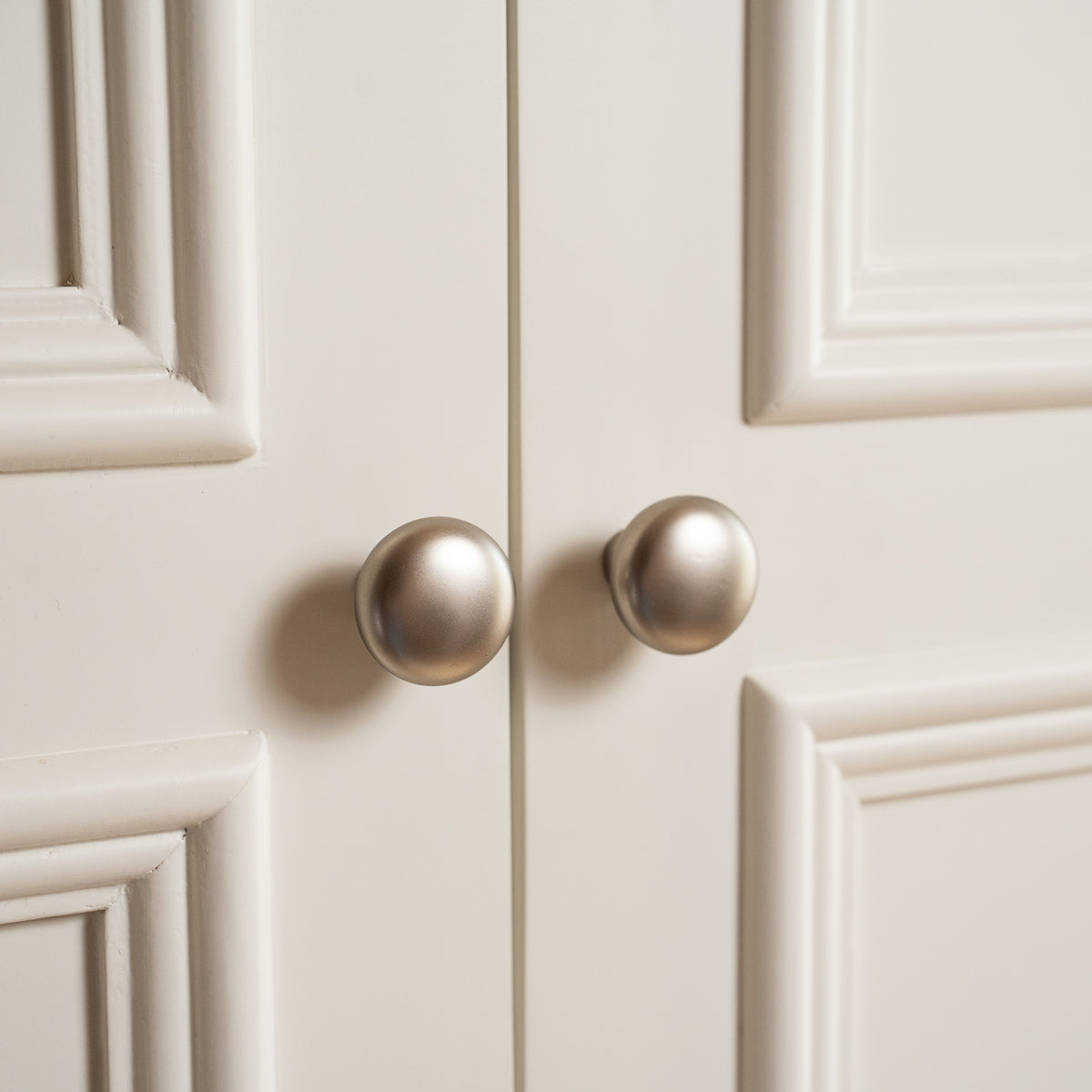 Close-up of two round, metallic cabinet knobs on the white paneled doors of the Amberley Double Wardrobe in Warm White, featuring a solid oak top.