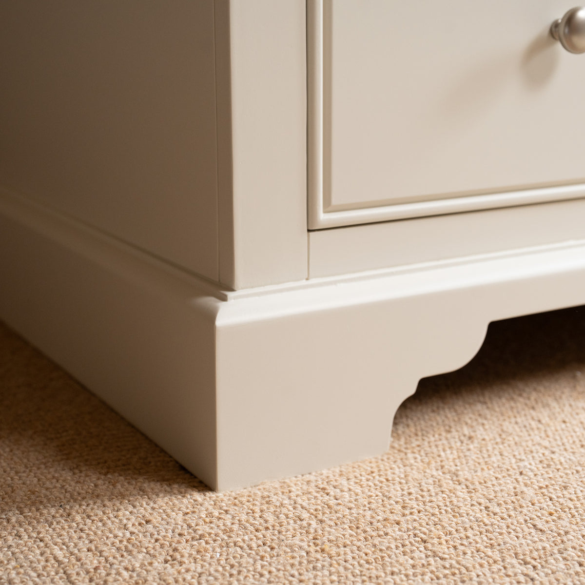 Close-up of the bottom corner of the Amberley Double Wardrobe in Warm White, featuring a solid oak top and set on a beige carpeted floor.