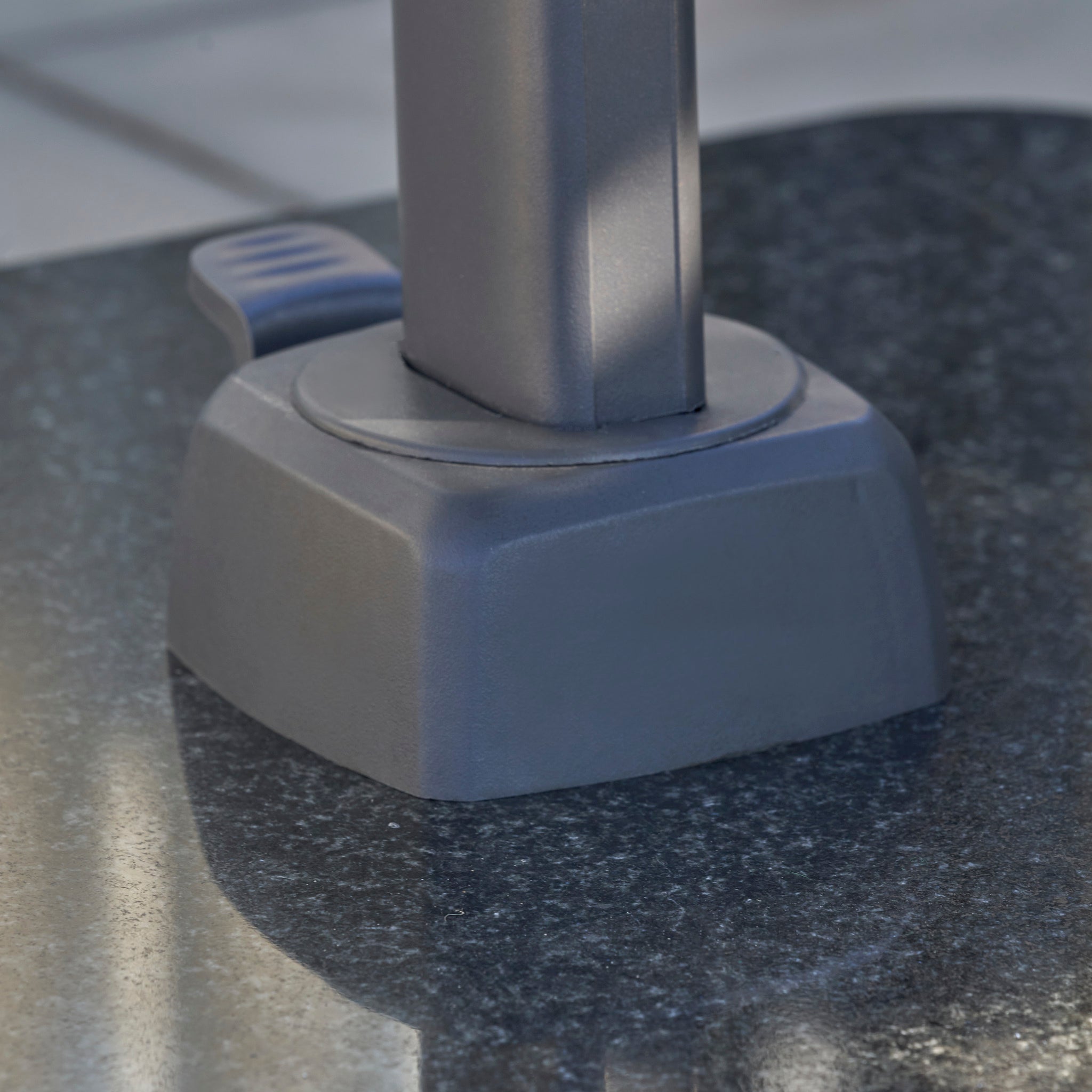 Close-up of a gray plastic umbrella stand base on a shiny dark stone surface, perfectly complementing the Voyager T2 2.7m Square Cantilever Parasol in Grey.