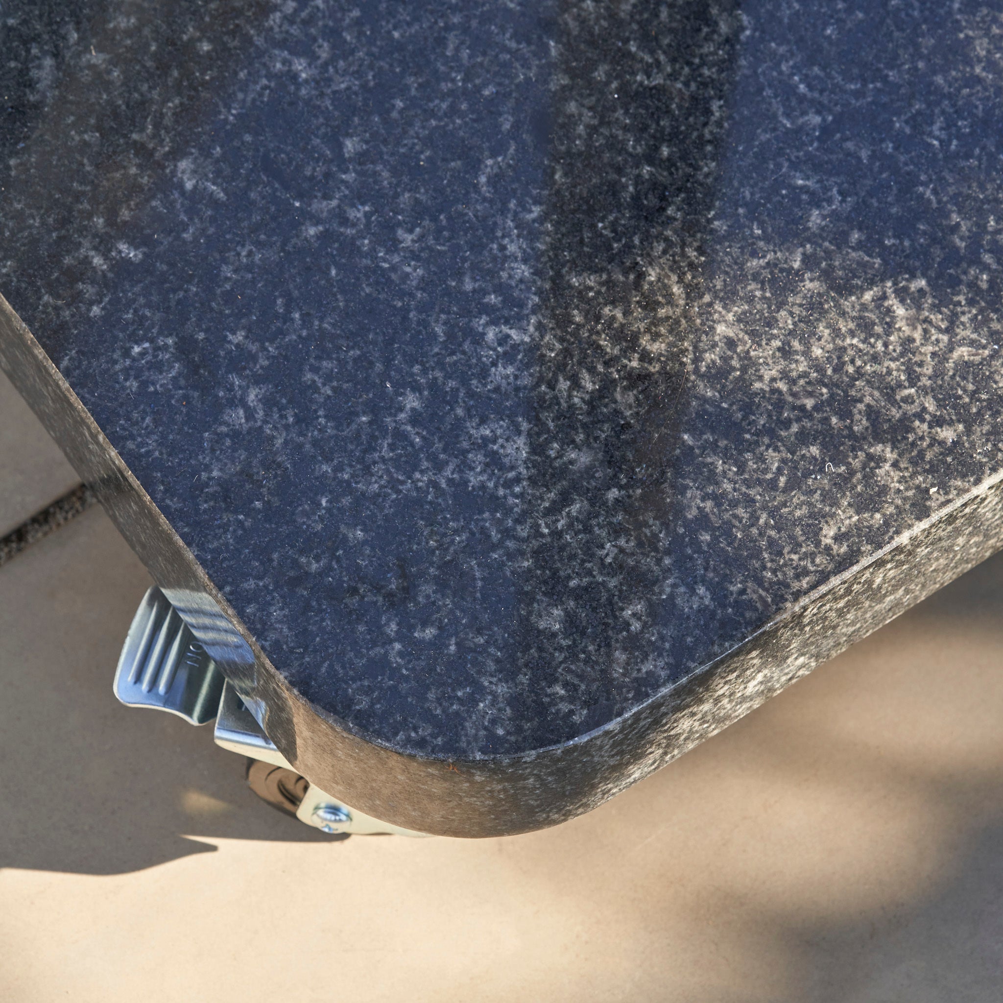 Close-up of the Ancona 90kg Granite Base with Wheels, showcasing its rounded edges, a sturdy metal wheel, and the wheel’s shadow on the tiled floor.