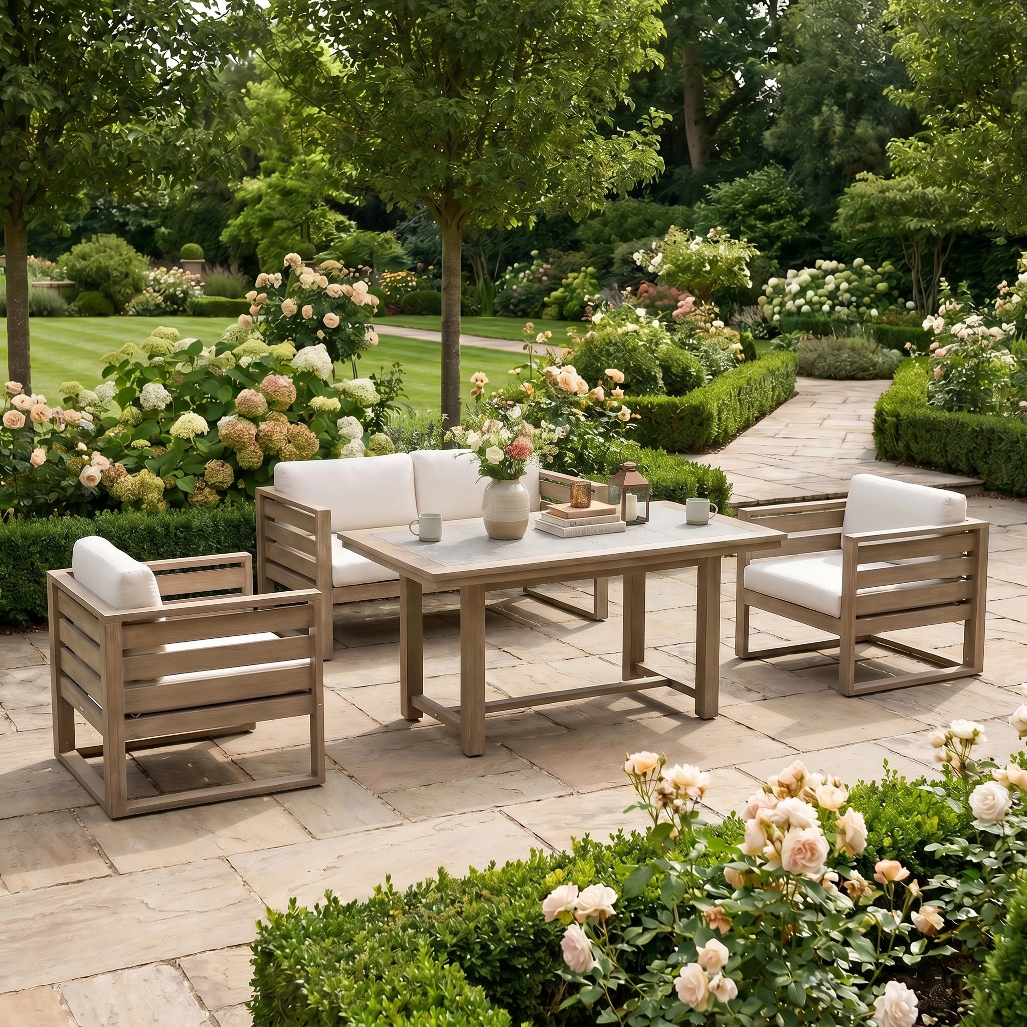 The Andora 2 Seat Sofa Set with 2 in 1 Table in Weathered Brown features wooden patio seating with white cushions, perfect for relaxing in style on a stone terrace surrounded by roses and lush gardens.