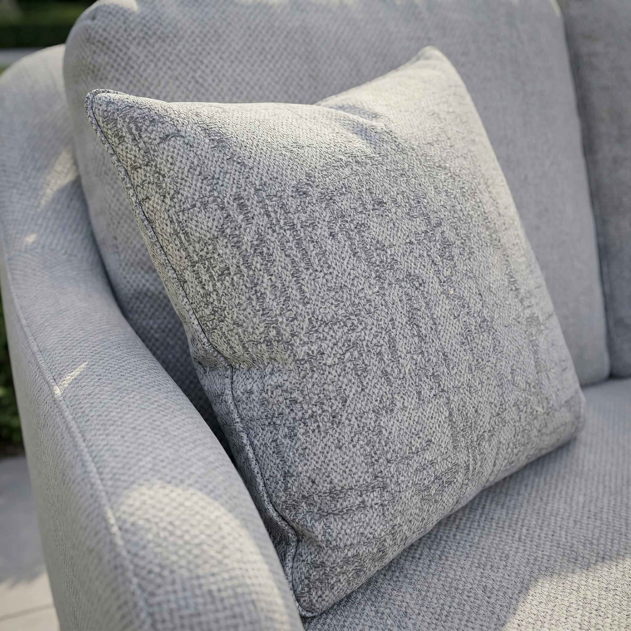 A close-up of the Agora Artisan Perla Medium Scatter Cushion (45cm x 45cm) in light gray on a matching outdoor armchair.