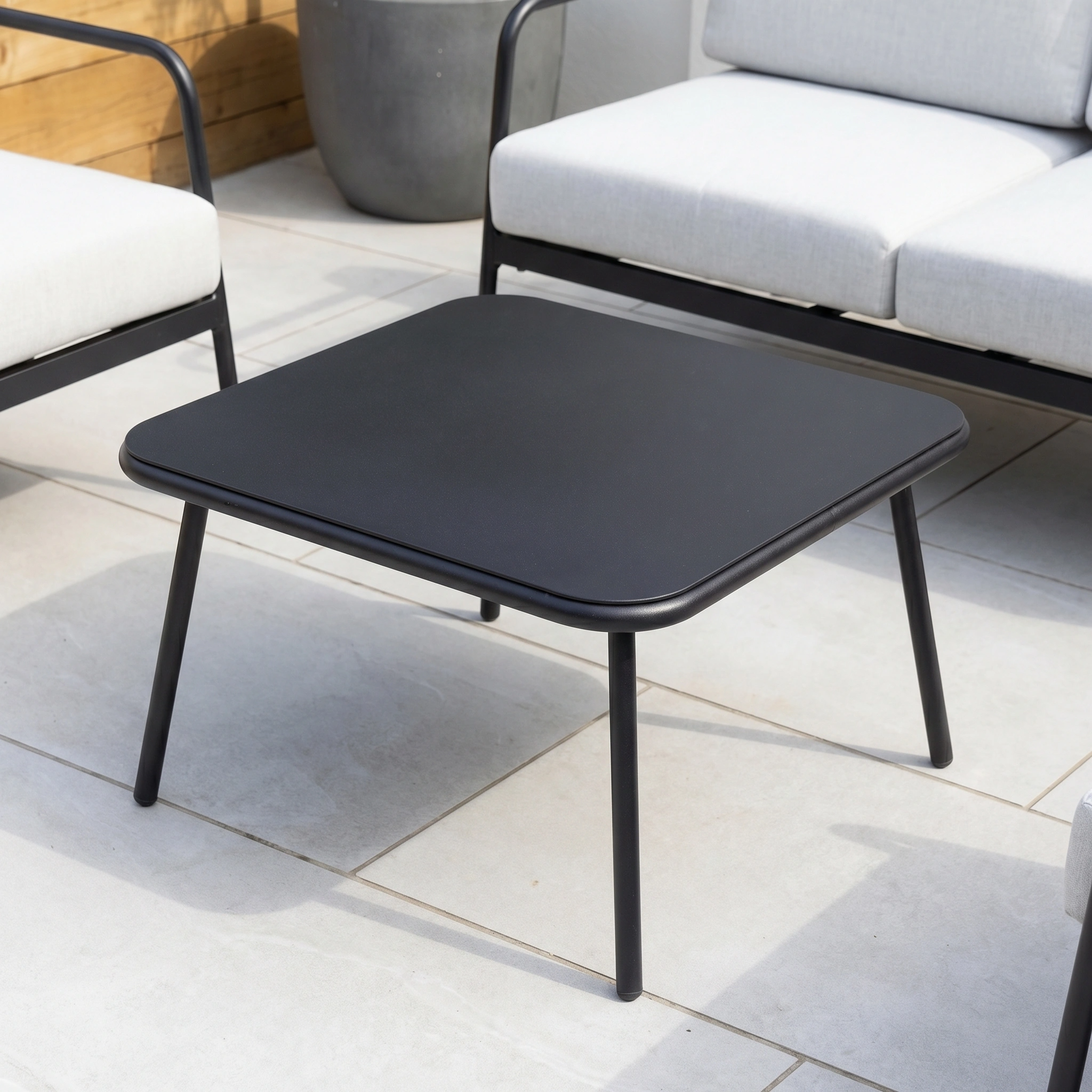 The Aspen 2 Seat Sofa with Coffee Table in Light Grey sits on a tiled patio, surrounded by cushioned chairs—an elegant, weather-resistant addition to any modern garden or patio furniture set.