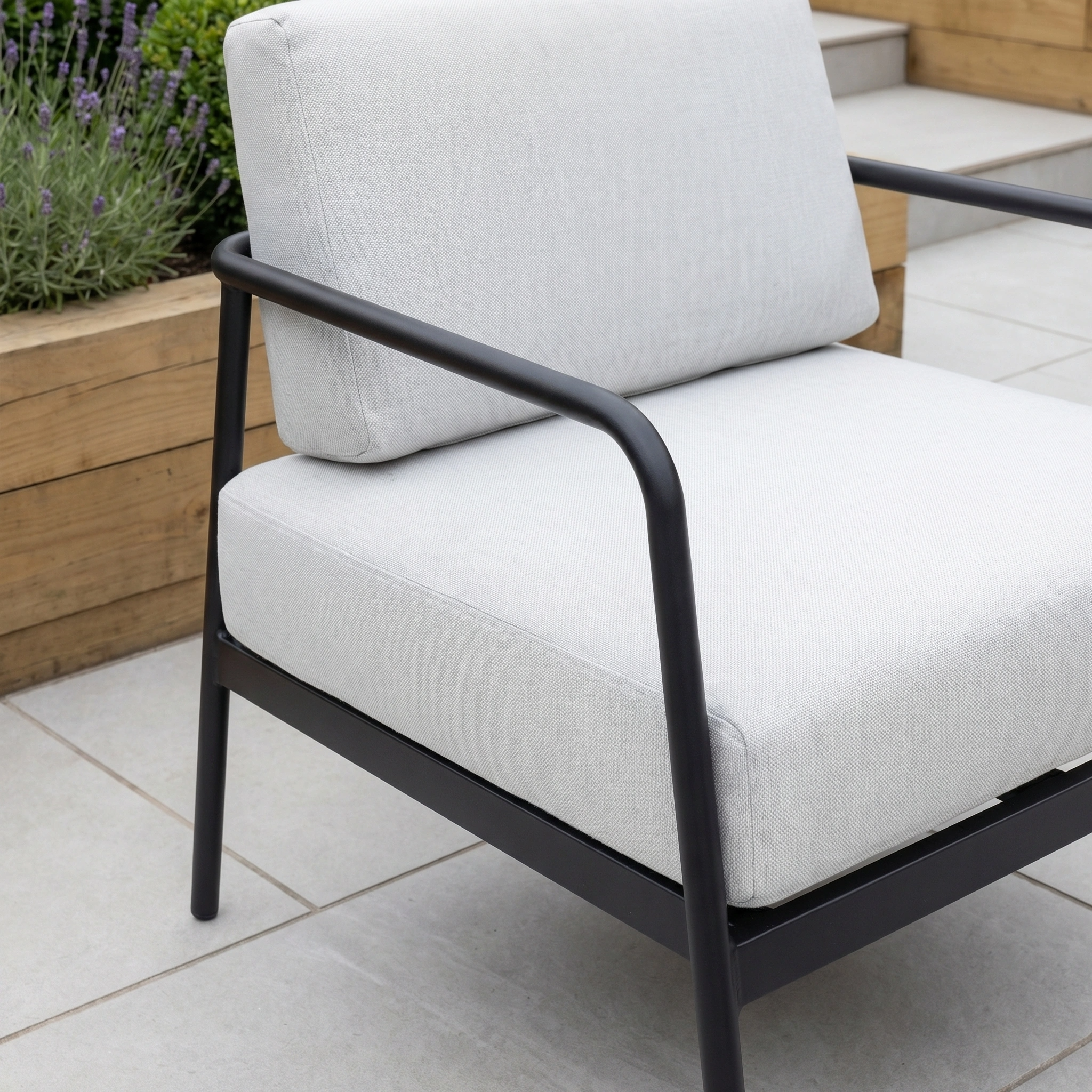 The Aspen 2 Seat Sofa with Coffee Table in Light Grey offers weather-resistant patio furniture with light grey cushions and a black metal frame, perfect for your tiled patio next to a wooden planter.