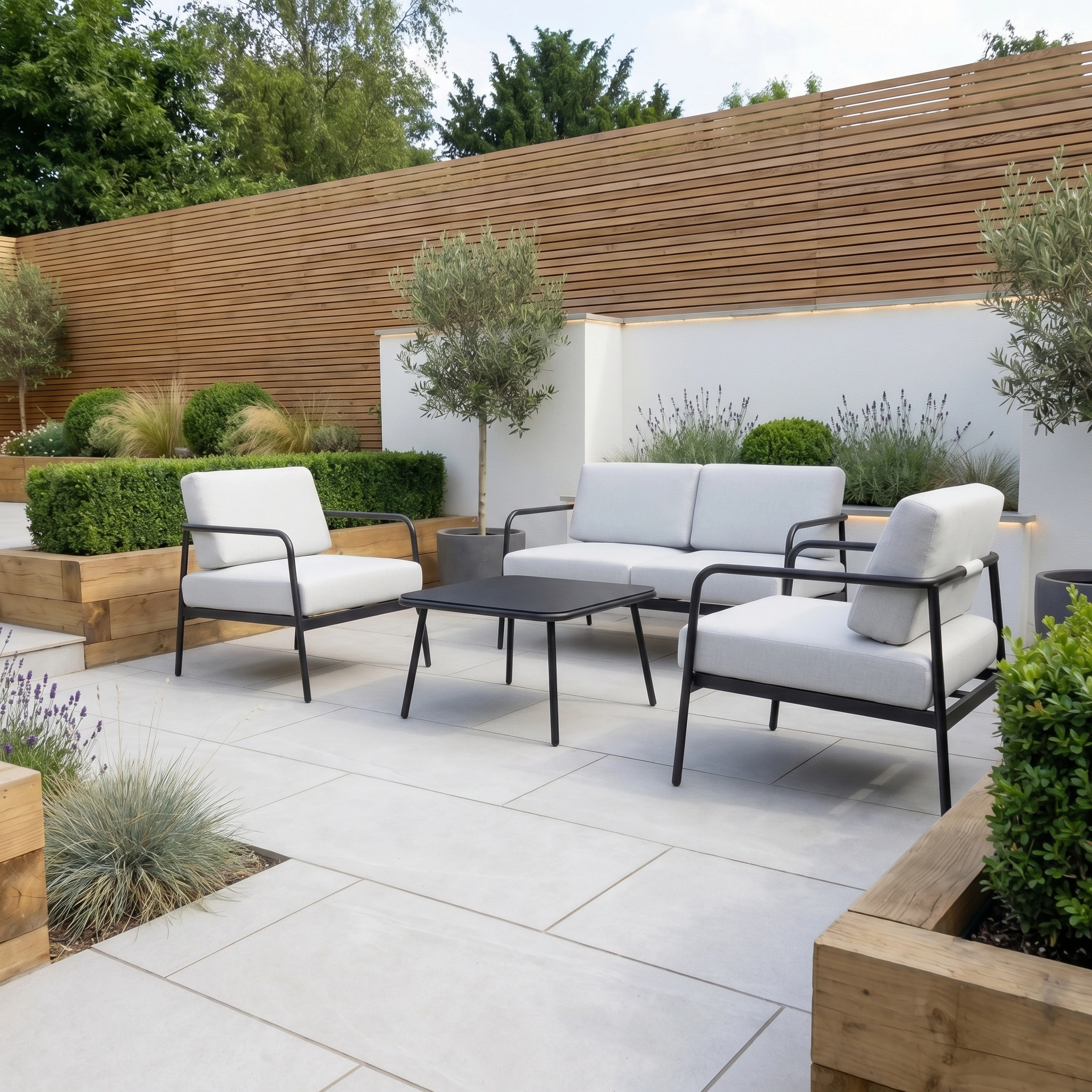Modern outdoor patio featuring the Aspen 2 Seat Sofa with Coffee Table in Light Grey, white cushioned seating, a sleek table, and wooden planters filled with lush greenery.