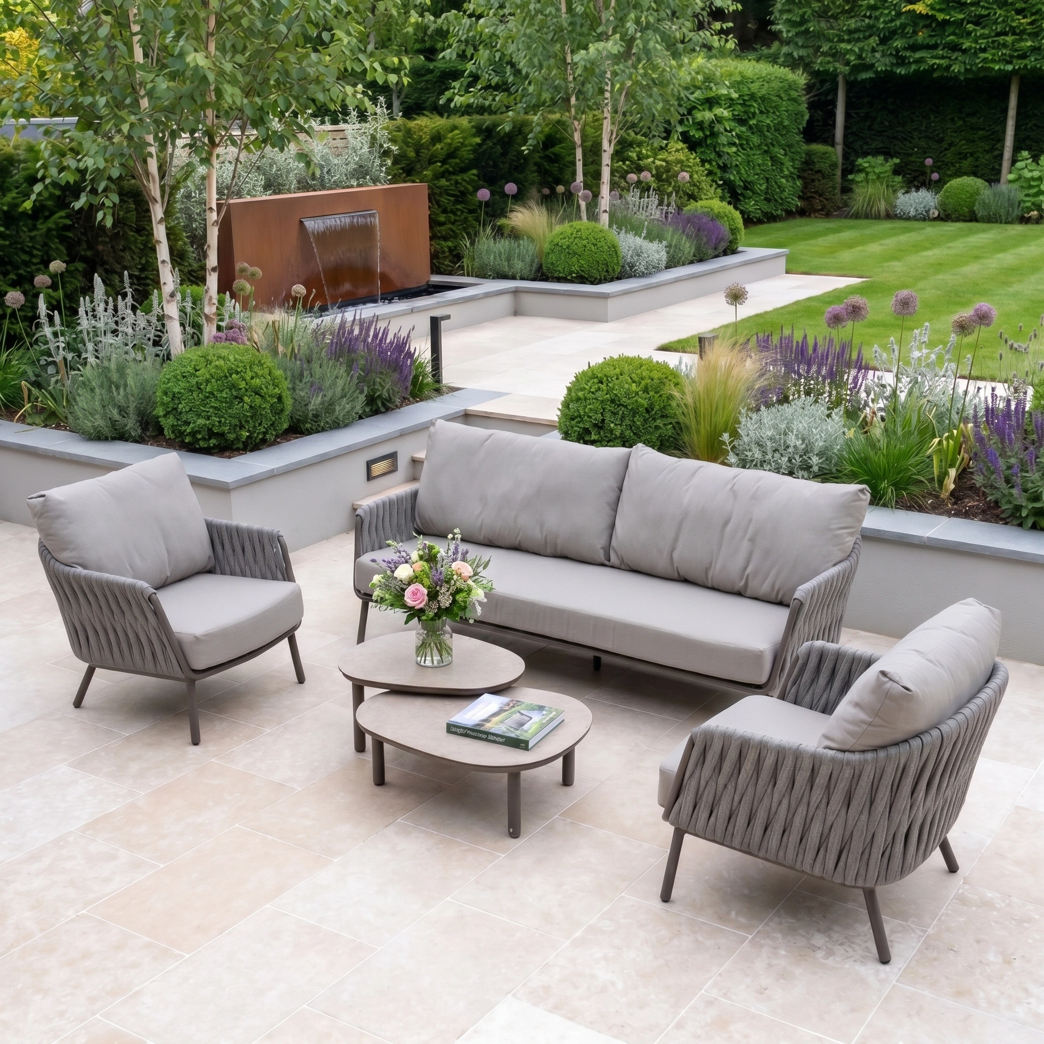 Modern patio with a Capri 3 Seat Sofa Set in Stone Grey, sleek outdoor furniture, matching coffee table, and a lush landscaped garden in the background.
