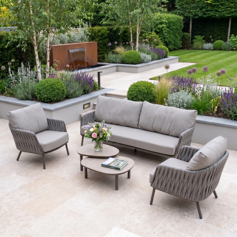 Modern patio with a Capri 3 Seat Sofa Set in Stone Grey, sleek outdoor furniture, matching coffee table, and a lush landscaped garden in the background.