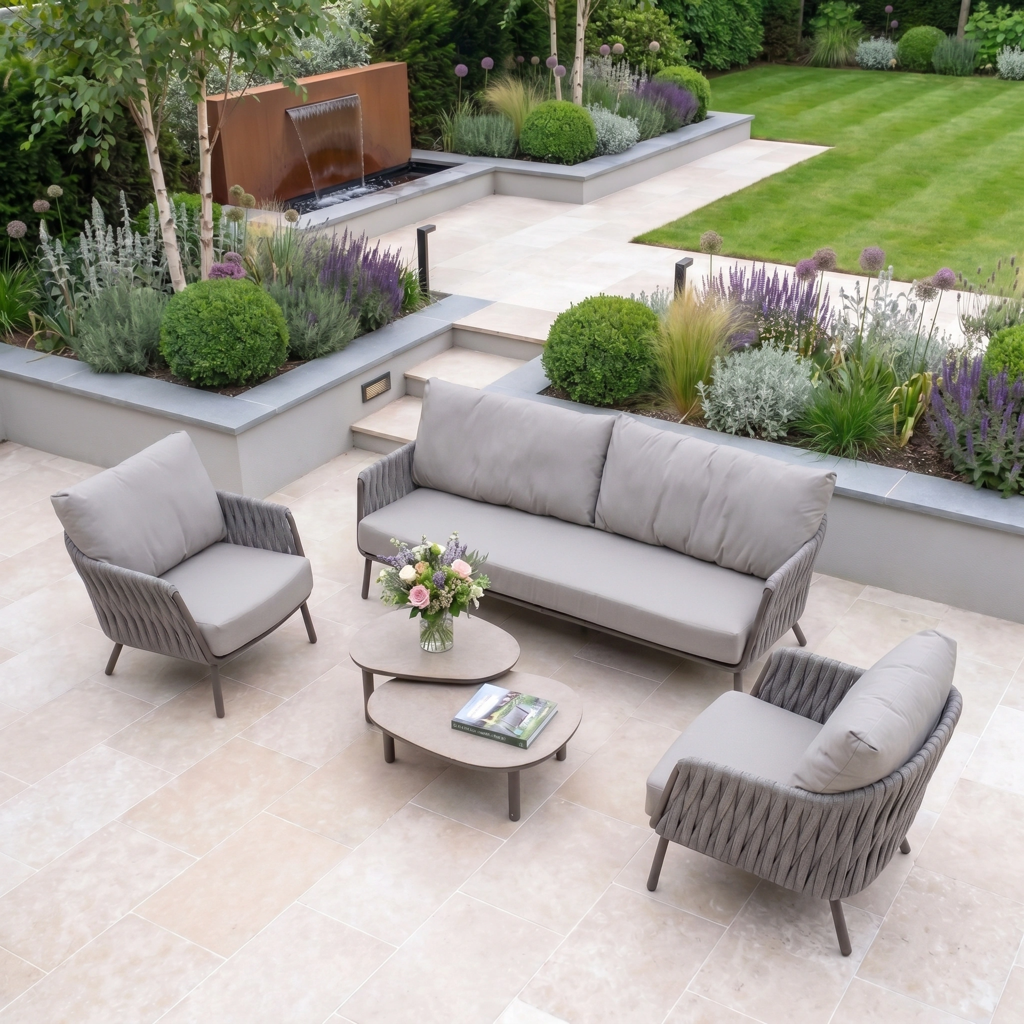 Modern outdoor patio featuring the Capri 3 Seat Sofa Set in Stone Grey, a coffee table, and a lush garden backdrop.