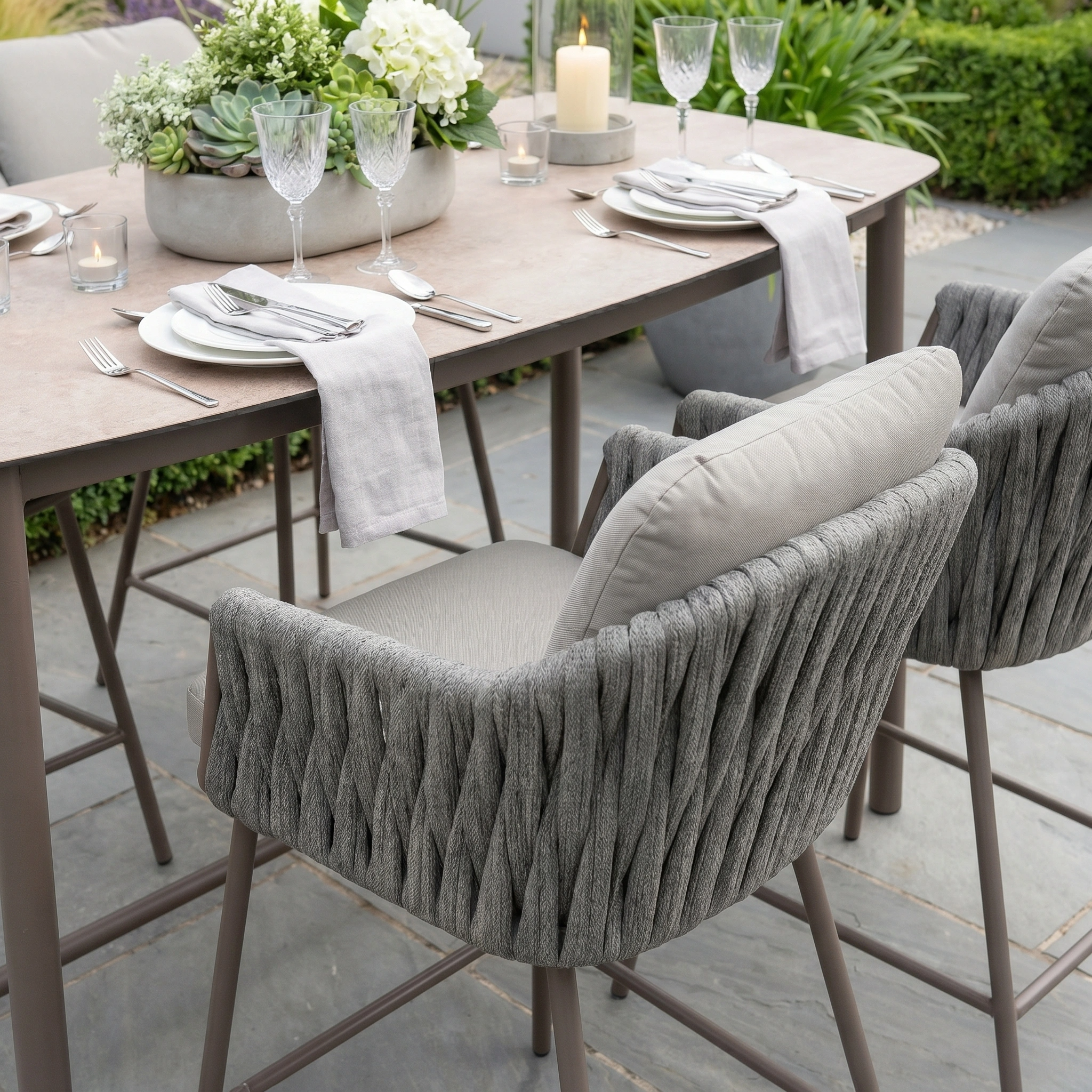Outdoor dining set with elegant place settings, crystal glasses, and woven gray chairs—expertly styled with the Capri 4 Seat High Rectangular Dining Set in Stone Grey for sophisticated alfresco gatherings.