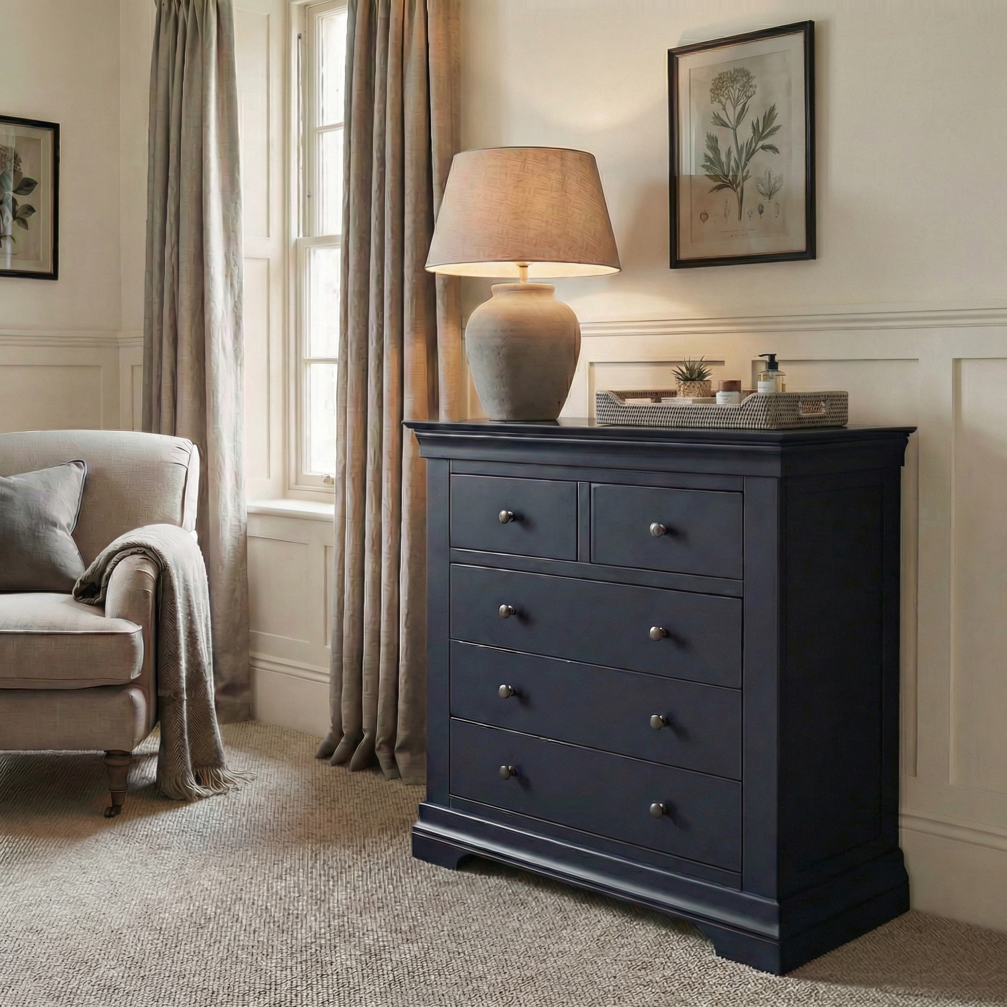 The Chalbury 2 Over 3 Chest of Drawers in Dusky Black, styled with a lamp, decor, and framed art, sits by a window in a cozy, neutral-toned room.