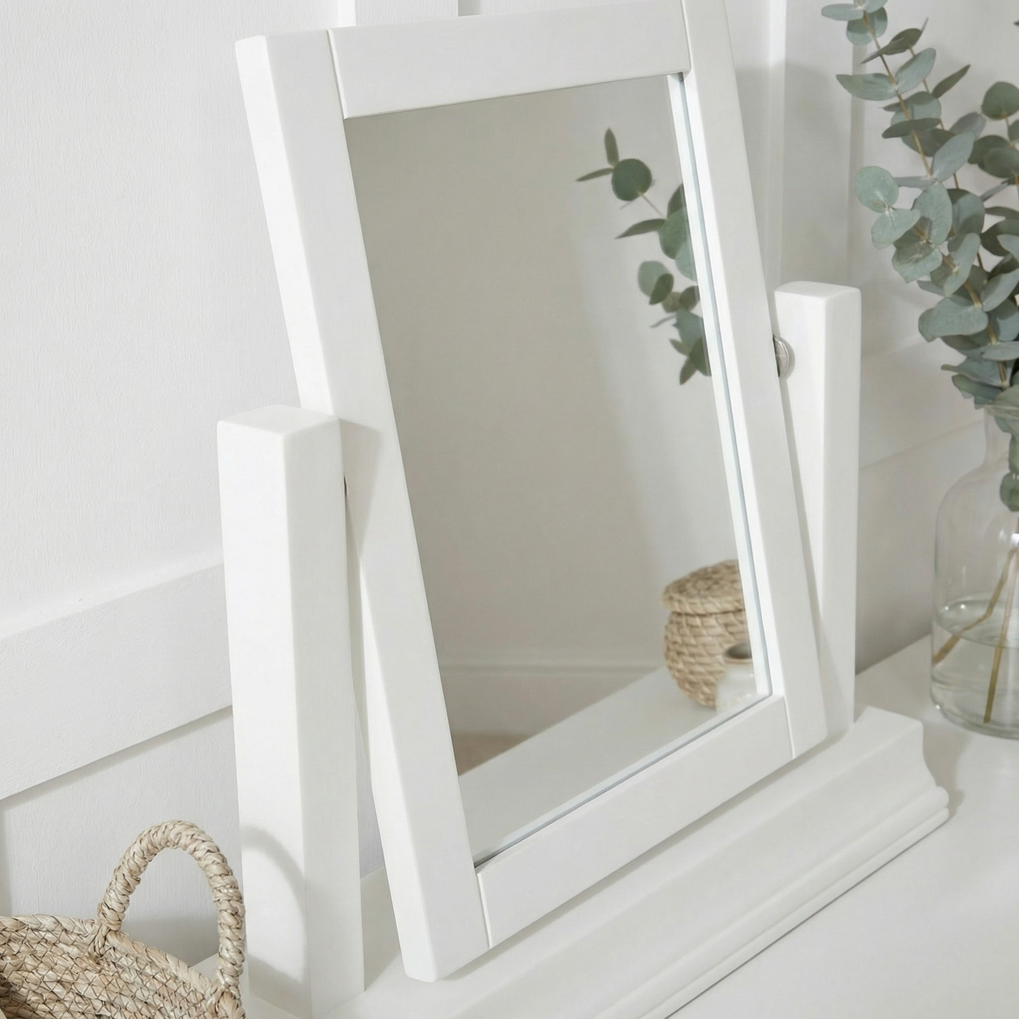 A Chalbury Mirror in Warm White tilts on a white surface, complemented by a wicker basket and eucalyptus vase for a fresh, modern vibe.