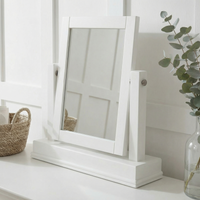 The Chalbury Mirror in Warm White features a rectangular frame and sits on a white surface beside a wicker basket and plant, bringing contemporary style to your space.