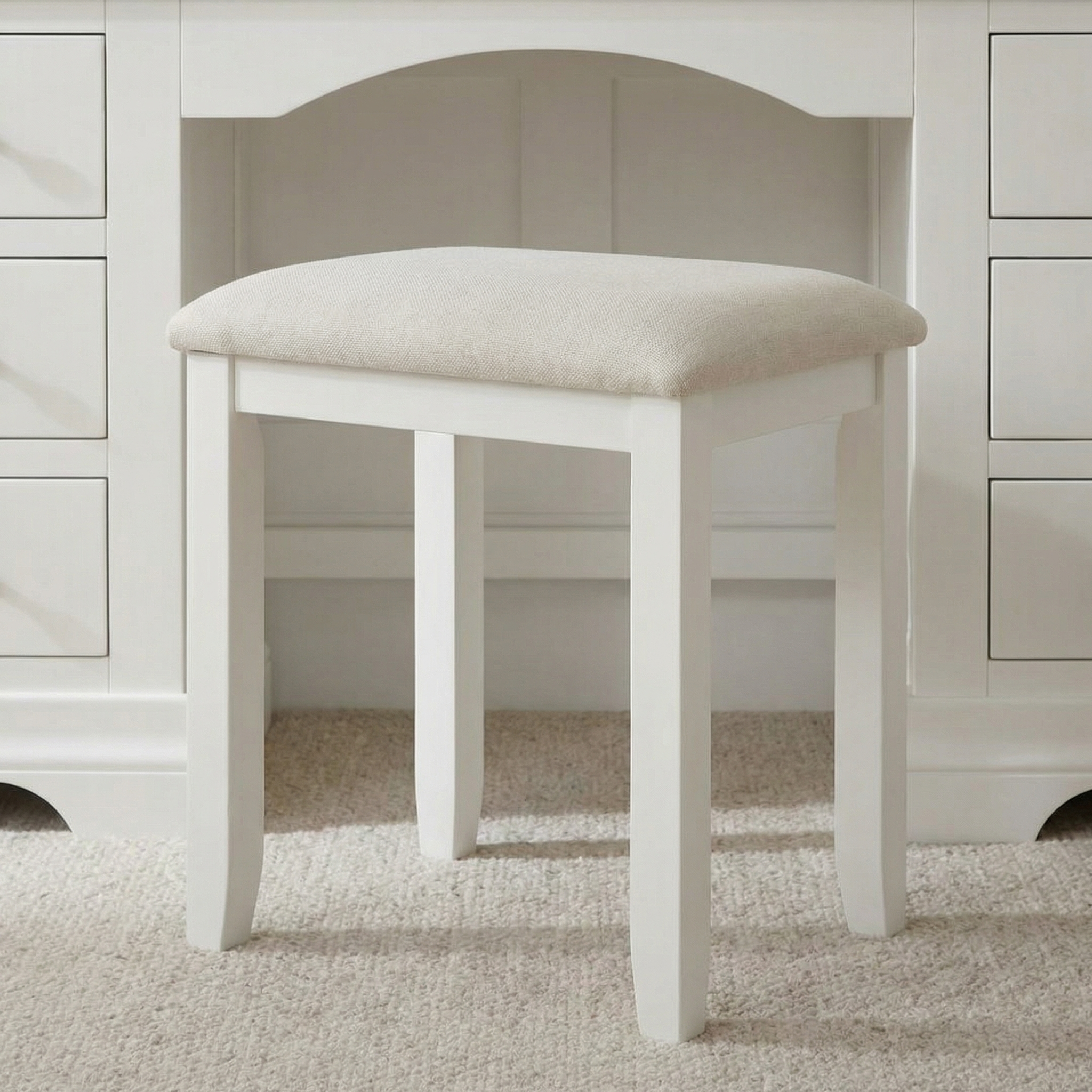The Chalbury Stool in Warm White features a built-in cushion and is shown placed on a carpet in front of a white desk.