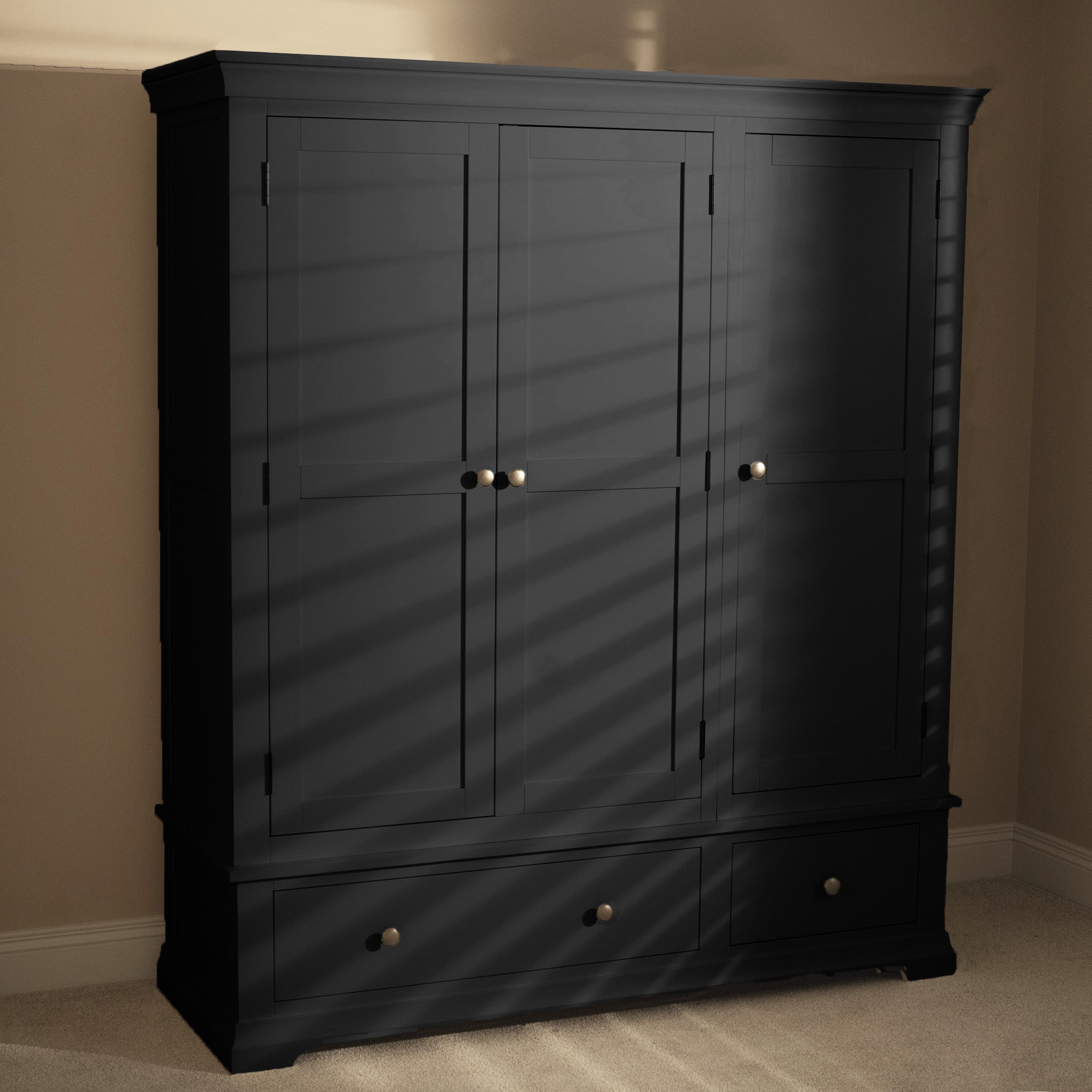 Sunlight streams through the blinds, highlighting the Chalbury Triple Wardrobe in Dusky Black with its closed doors and drawers, adding a contemporary touch to the room.