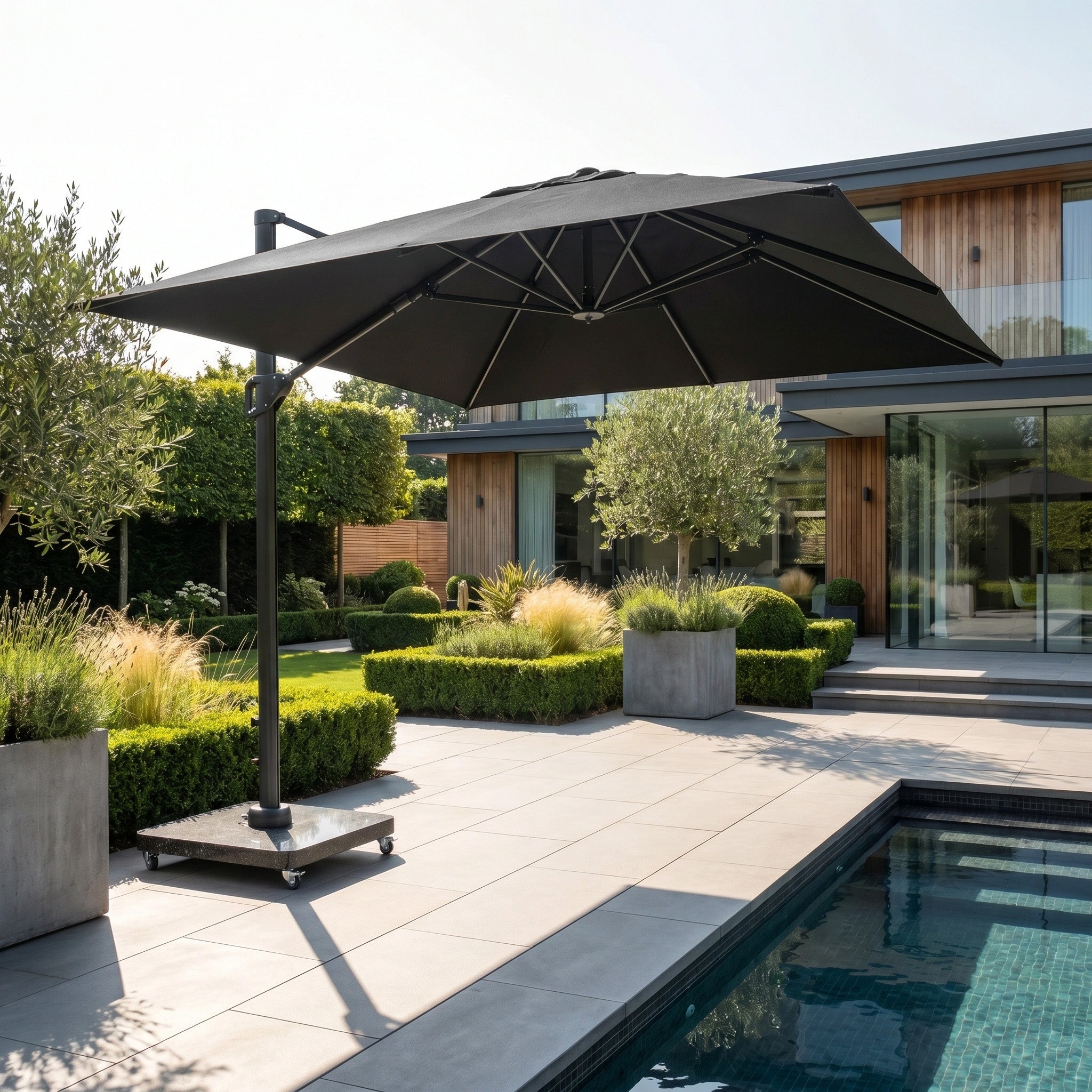 The Challenger T2 Premium 3.5m x 2.6m Rectangular Cantilever Parasol in Black stands by a modern backyard pool, surrounded by lush plants and a contemporary house in the background.