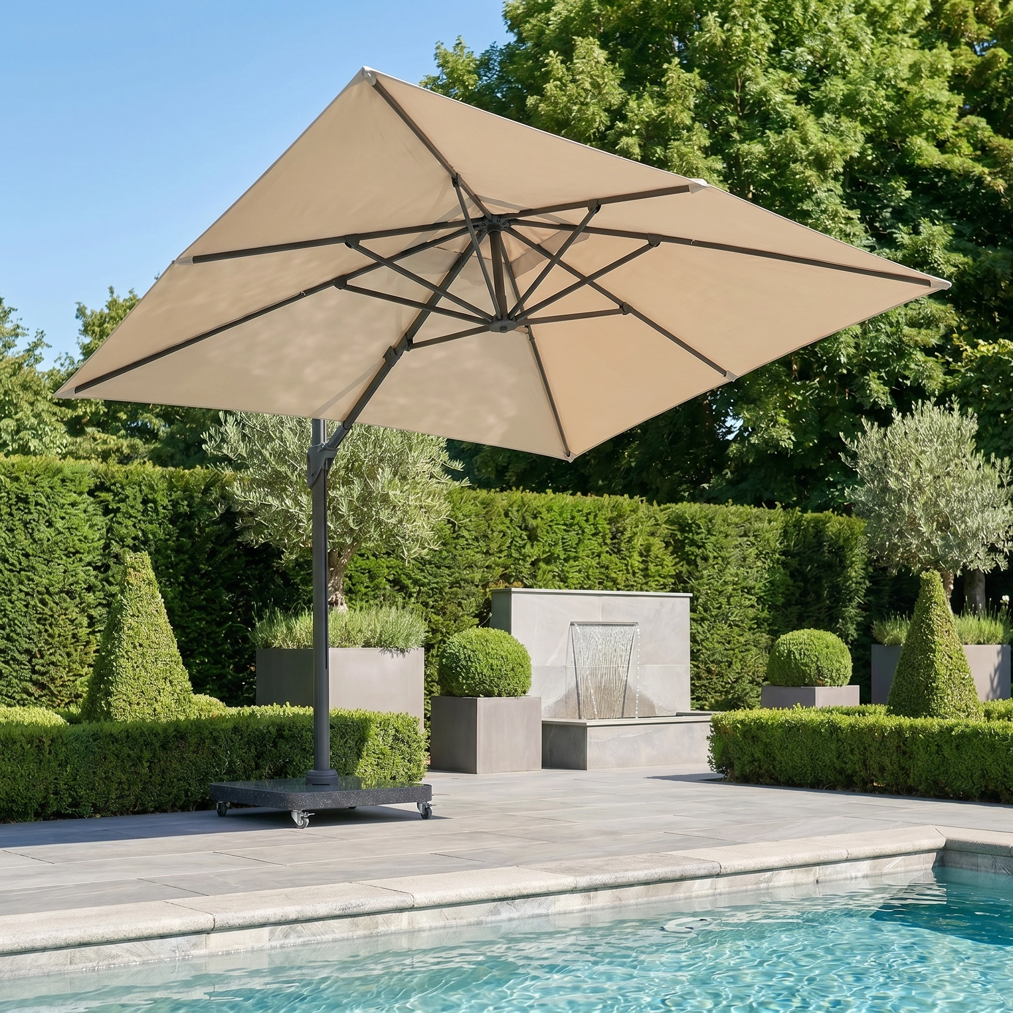 The Challenger T2 Premium 3.5m x 2.6m Rectangular Cantilever Parasol in Champagne shades the poolside area, complemented by lush greenery, manicured hedges, and a decorative water feature in the background.