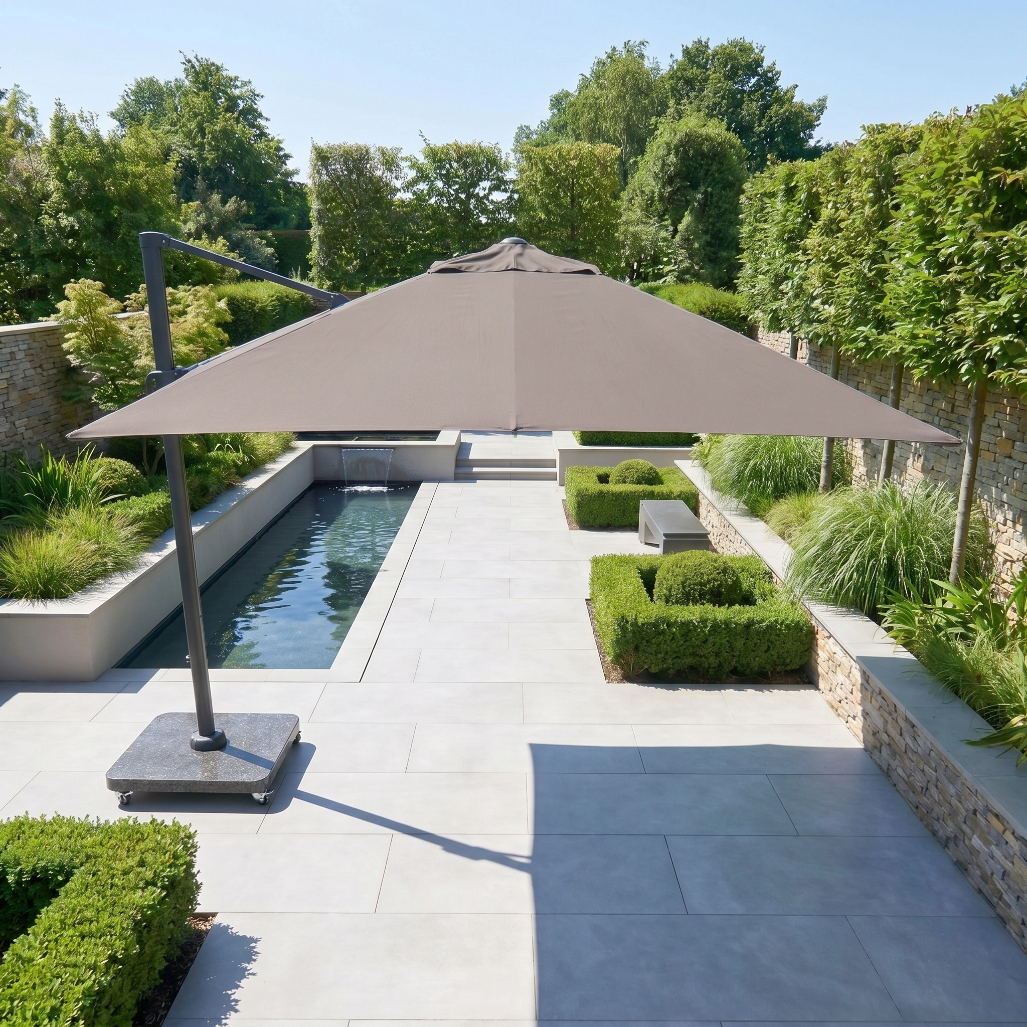 The Challenger T2 Premium 3.5m x 2.6m Rectangular Cantilever Parasol in Deep Taupe shades a modern garden featuring a pool, stone paving, and well-kept greenery.