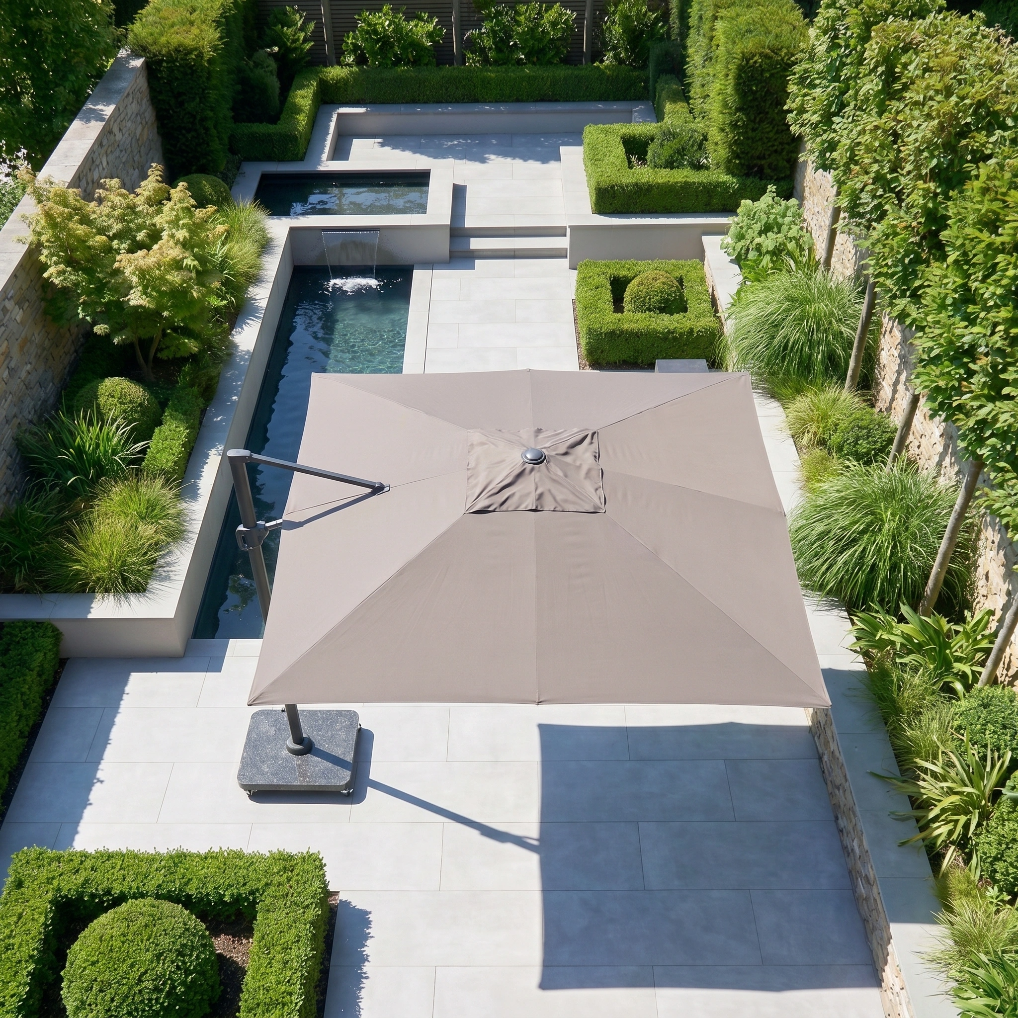 Modern garden with tiled patio, lush green plants, a narrow water feature, and the Challenger T2 Premium 3.5m x 2.6m Rectangular Cantilever Parasol in Deep Taupe for stylish outdoor shade.
