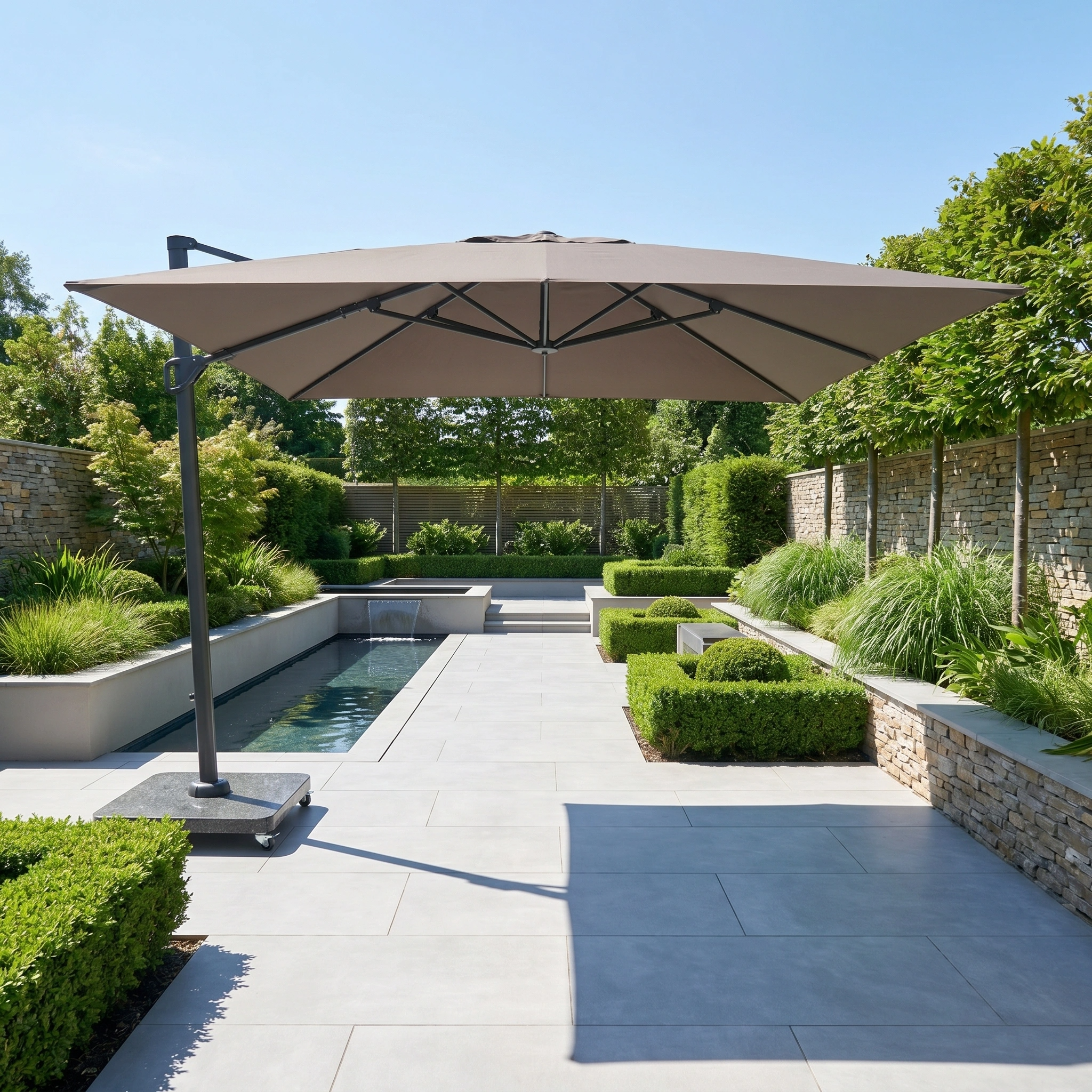 Modern backyard patio with the Challenger T2 Premium 3.5m x 2.6m Rectangular Cantilever Parasol in Deep Taupe providing outdoor shade, set by a pool, lush greenery, and stone walls on a sunny day.