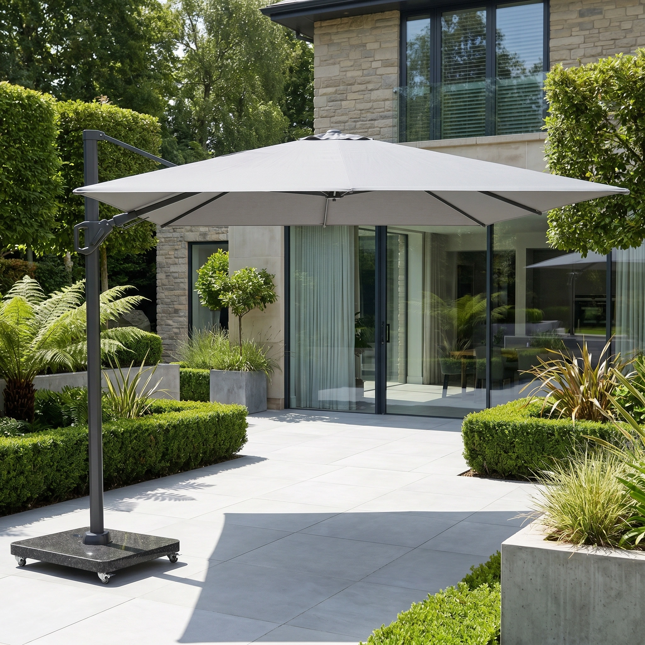 The Challenger T2 Premium 3.5m x 2.6m Rectangular Cantilever Parasol in Manhattan Grey offers elegant outdoor shade on a tiled terrace, blending seamlessly with modern greenery outside a contemporary home.