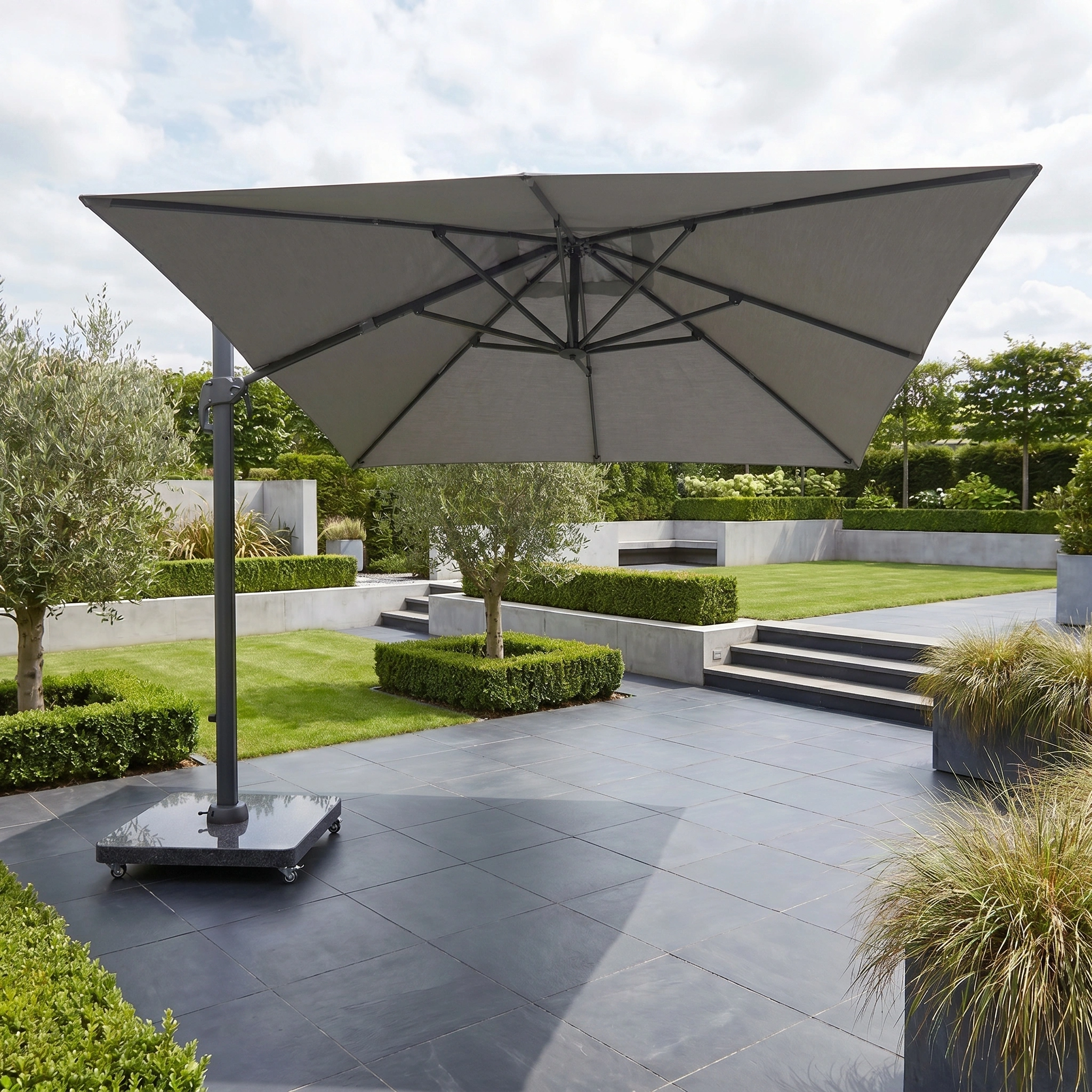 The Challenger T2 Premium 3.5m x 2.6m Rectangular Cantilever Parasol in Manhattan Grey offers stylish outdoor shade over modern stone tiles, steps, and lush greenery in your landscaped garden.