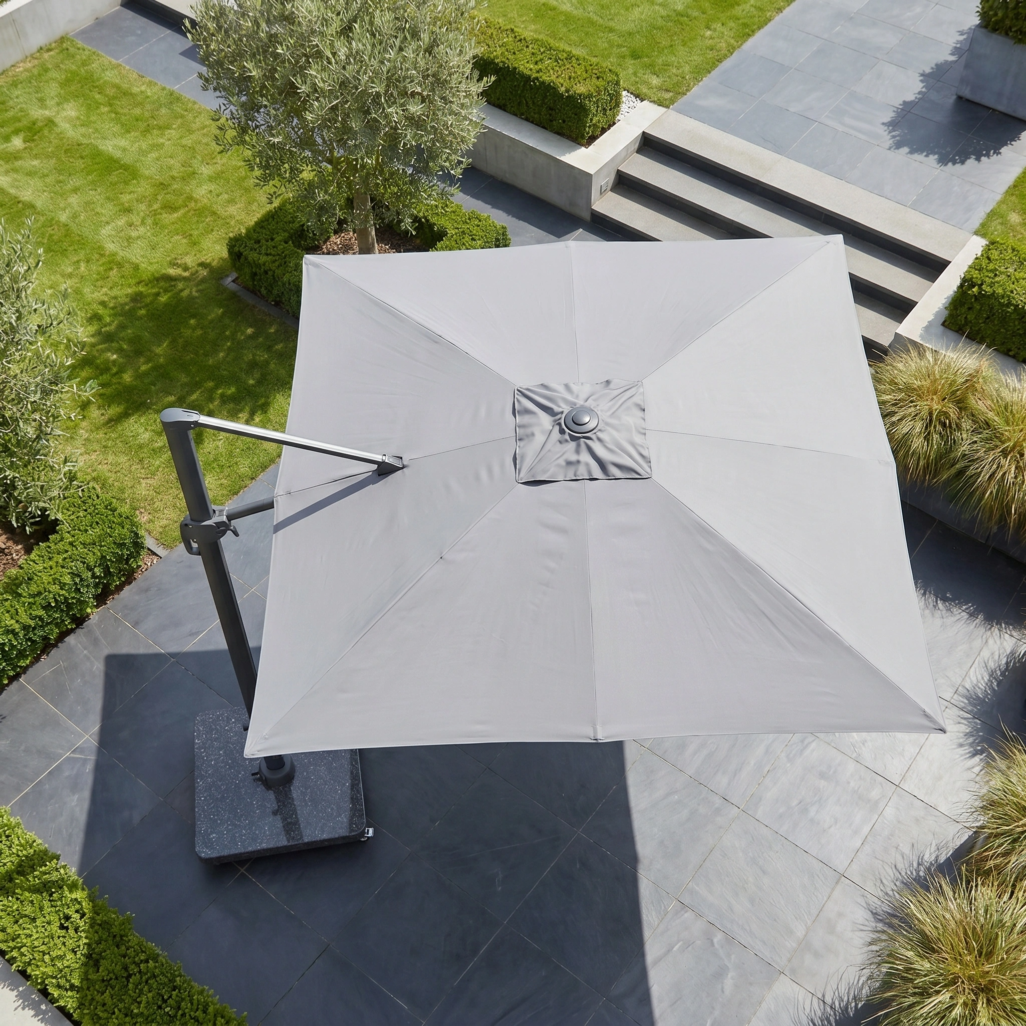 The Challenger T2 Premium 3.5m x 2.6m Rectangular Cantilever Parasol in Manhattan Grey offers stylish outdoor shade for a modern garden with stone tiles and green hedges.