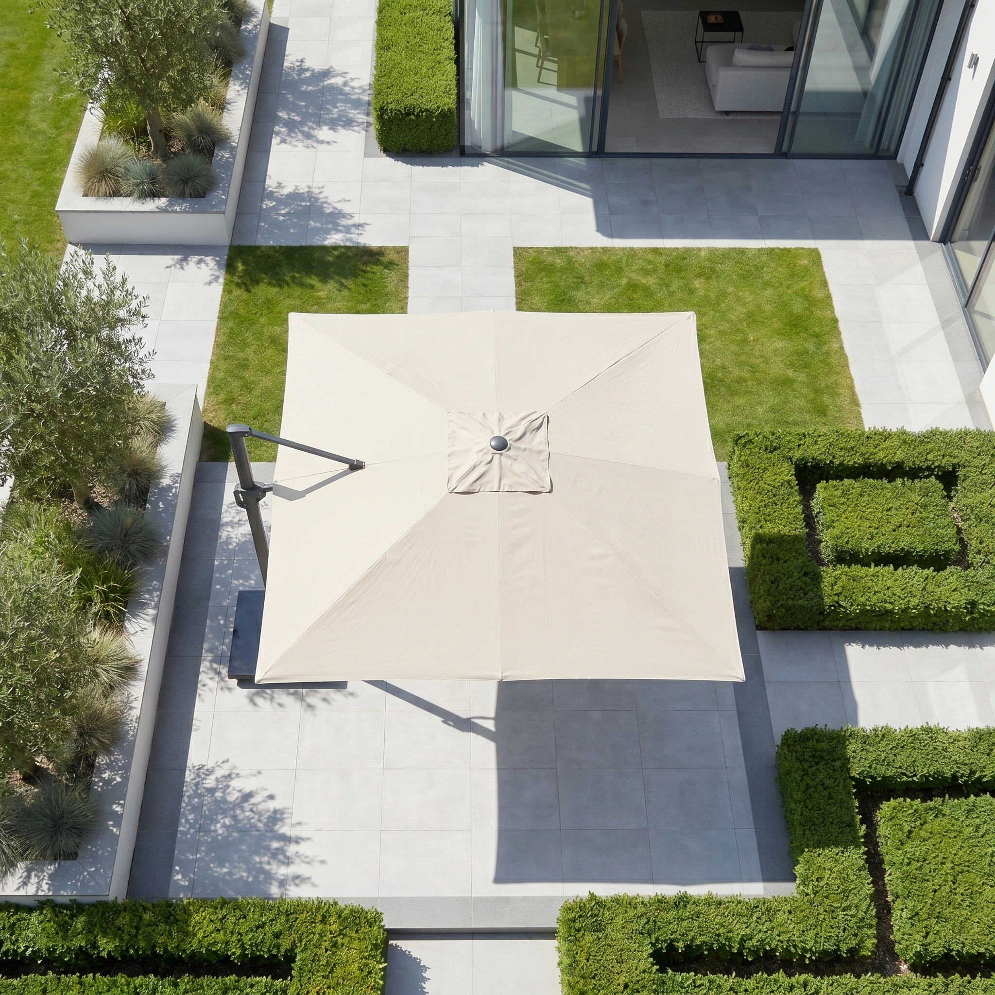 The Challenger T2 3.5m x 2.6m Rectangular Cantilever Parasol in Champagne shades a modern, tiled outdoor area bordered by geometric green hedges.