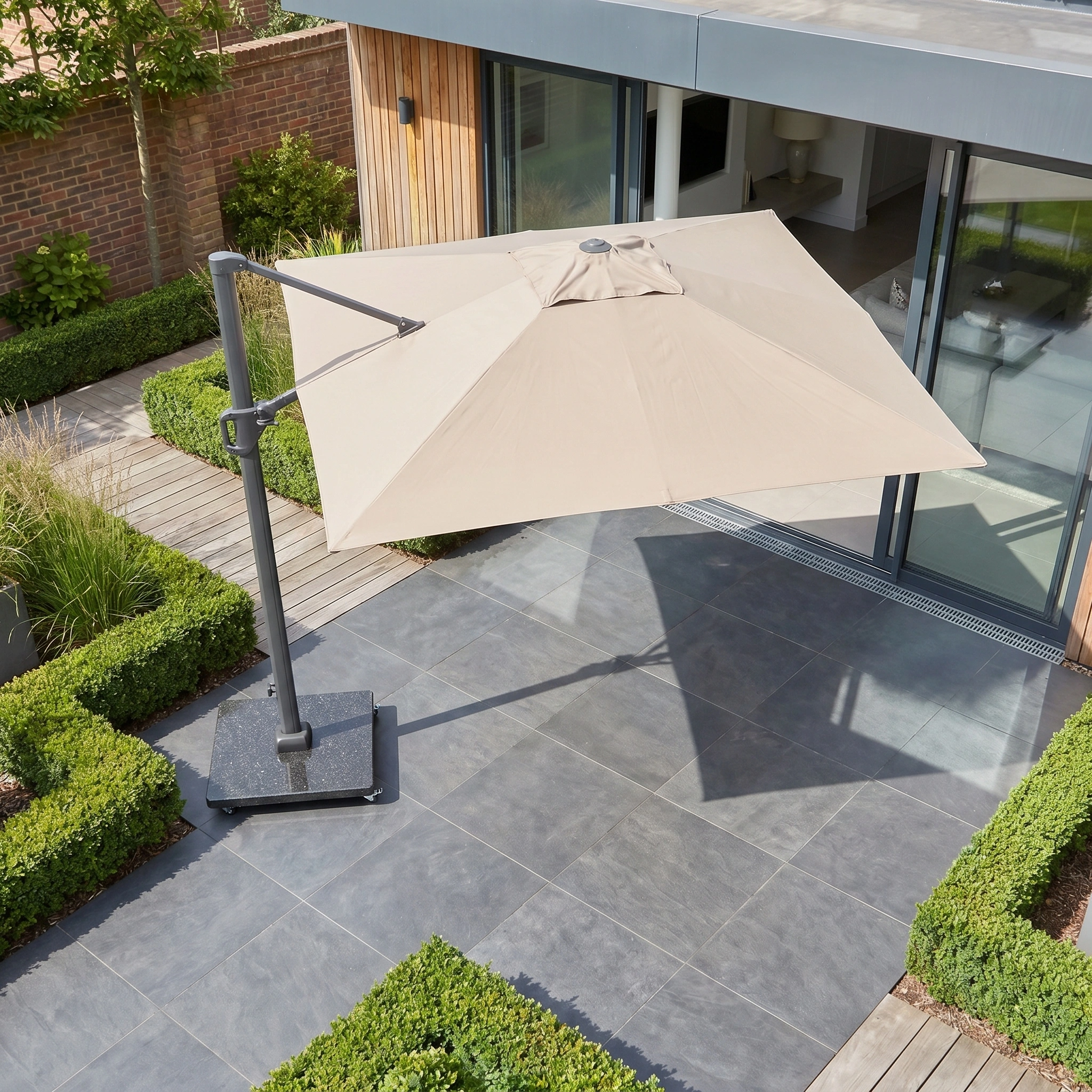The Challenger T2 3.5m x 2.6m Rectangular Cantilever Parasol in Taupe with 90kg Granite Base shades a tiled patio by a modern home, blending style and premium UV protection for your outdoor space.